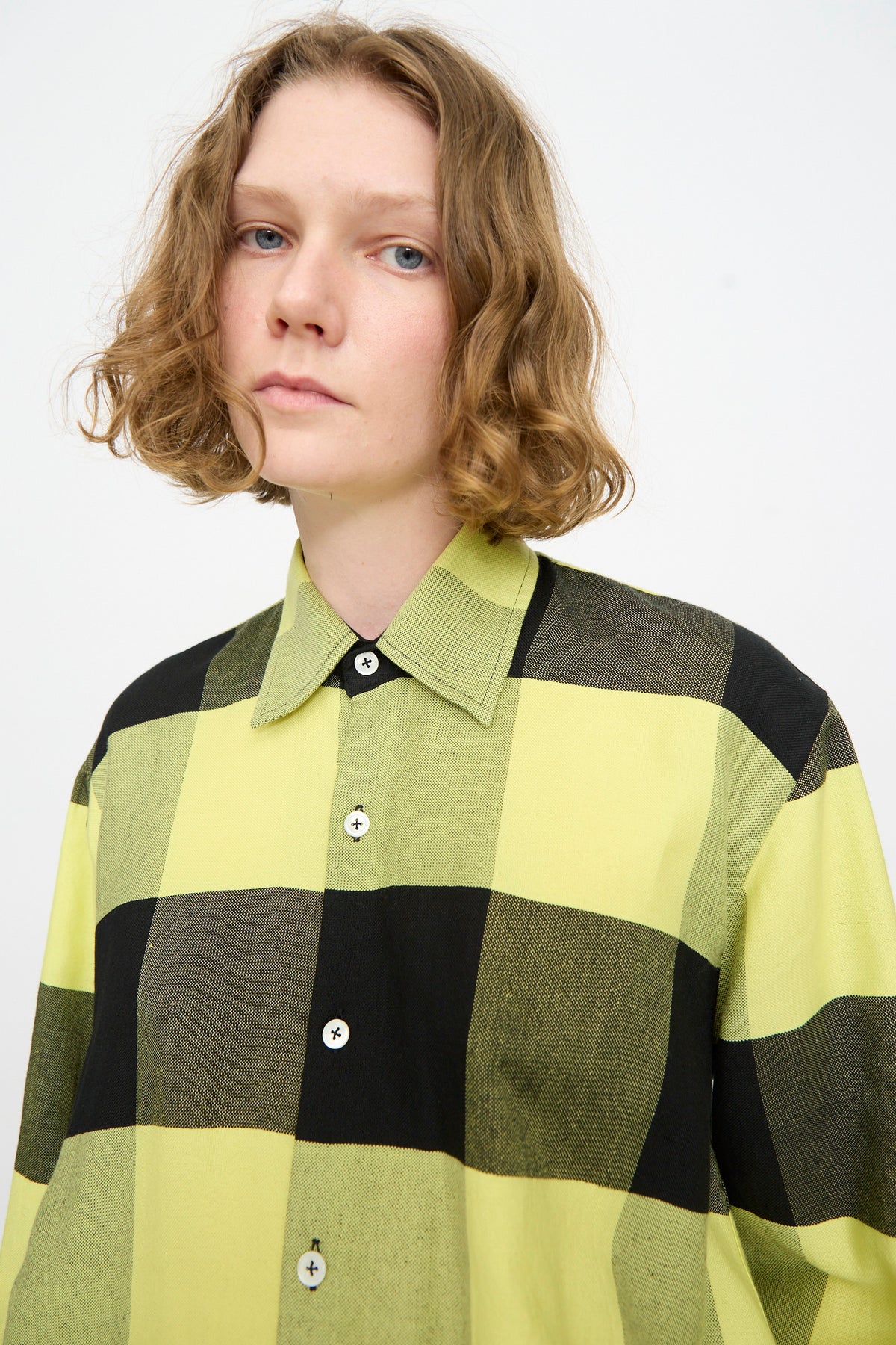 A person with short curly hair is wearing the Marrakshi Life French Cuff Shirt in Plaid Black and Sunny, standing against a plain white background.
