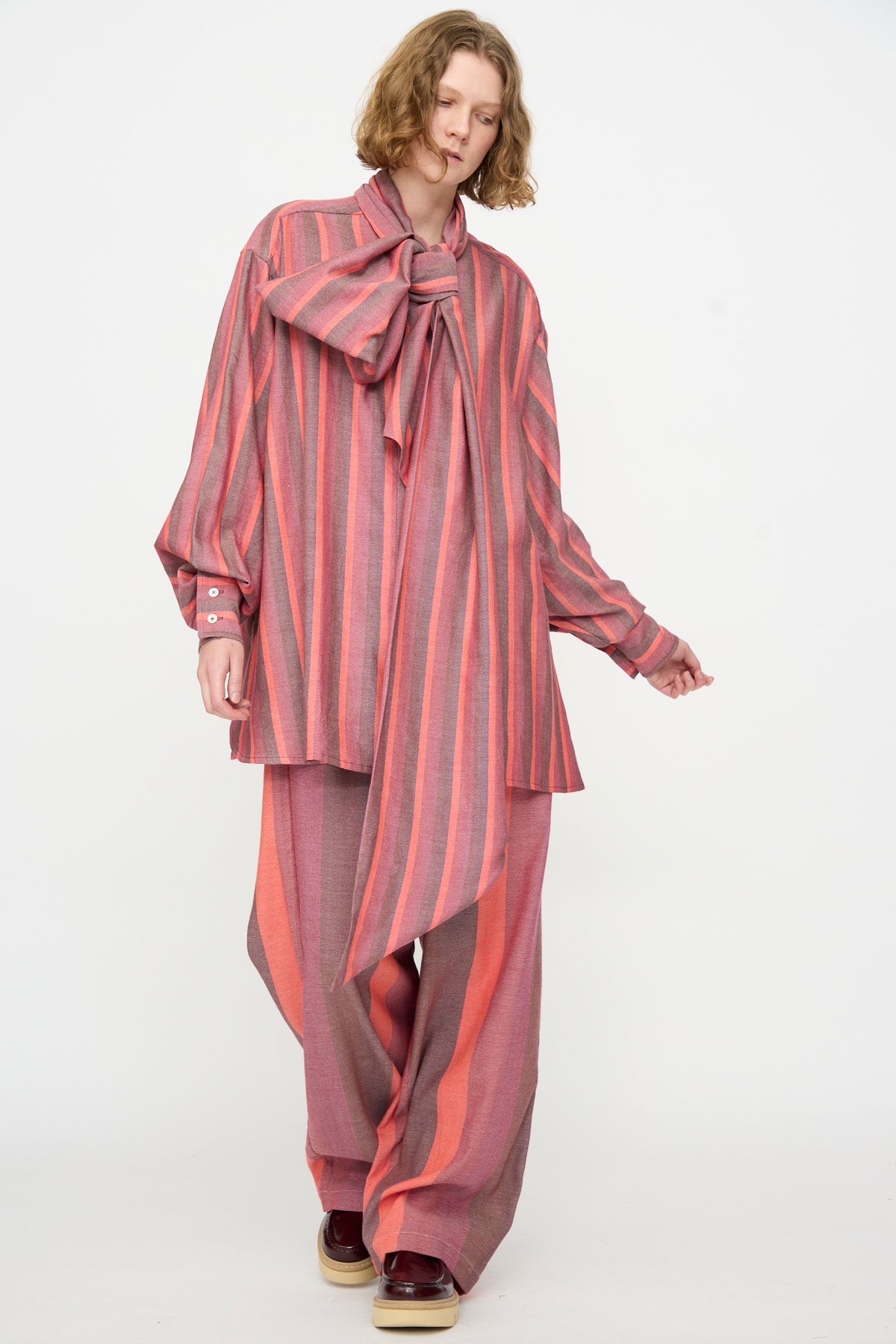 A person wearing The Parachute Pant in Stripe Multi by Marrakshi Life—a handwoven cotton, oversized pink and red striped set featuring a large bow—stands against a plain white background.