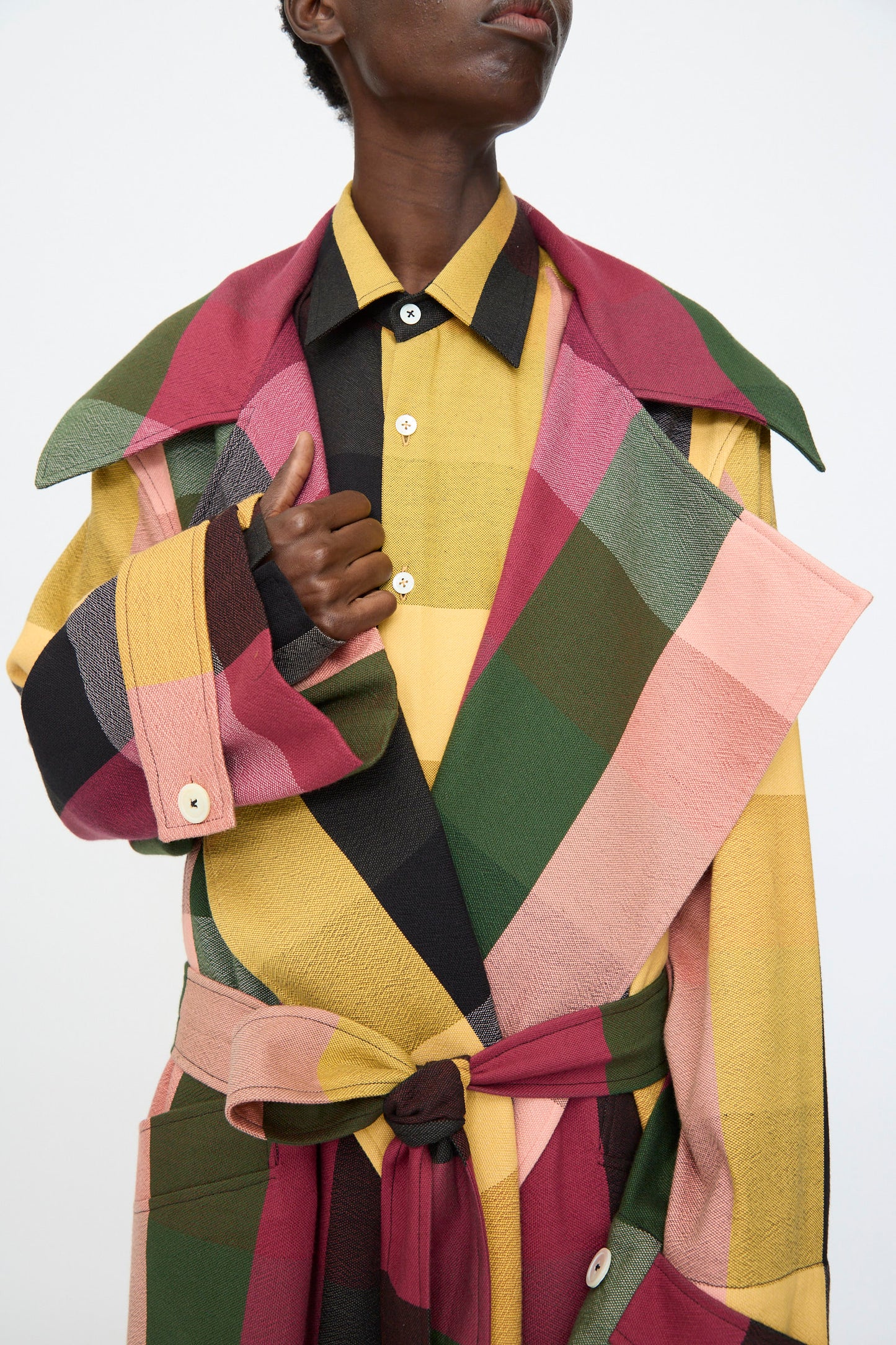 A person wears the Marrakshi Life Trench Coat in Plaid Multi with a matching belt over a yellow plaid shirt, standing against a plain background.