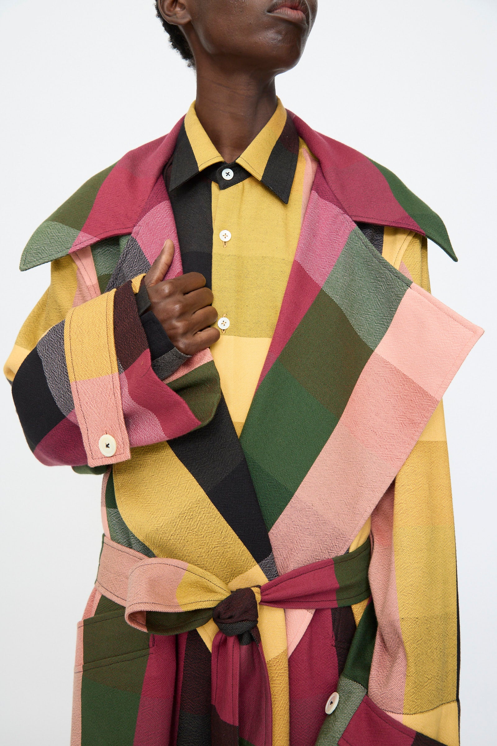 A person wears the Marrakshi Life Trench Coat in Plaid Multi with a matching belt over a yellow plaid shirt, standing against a plain background.