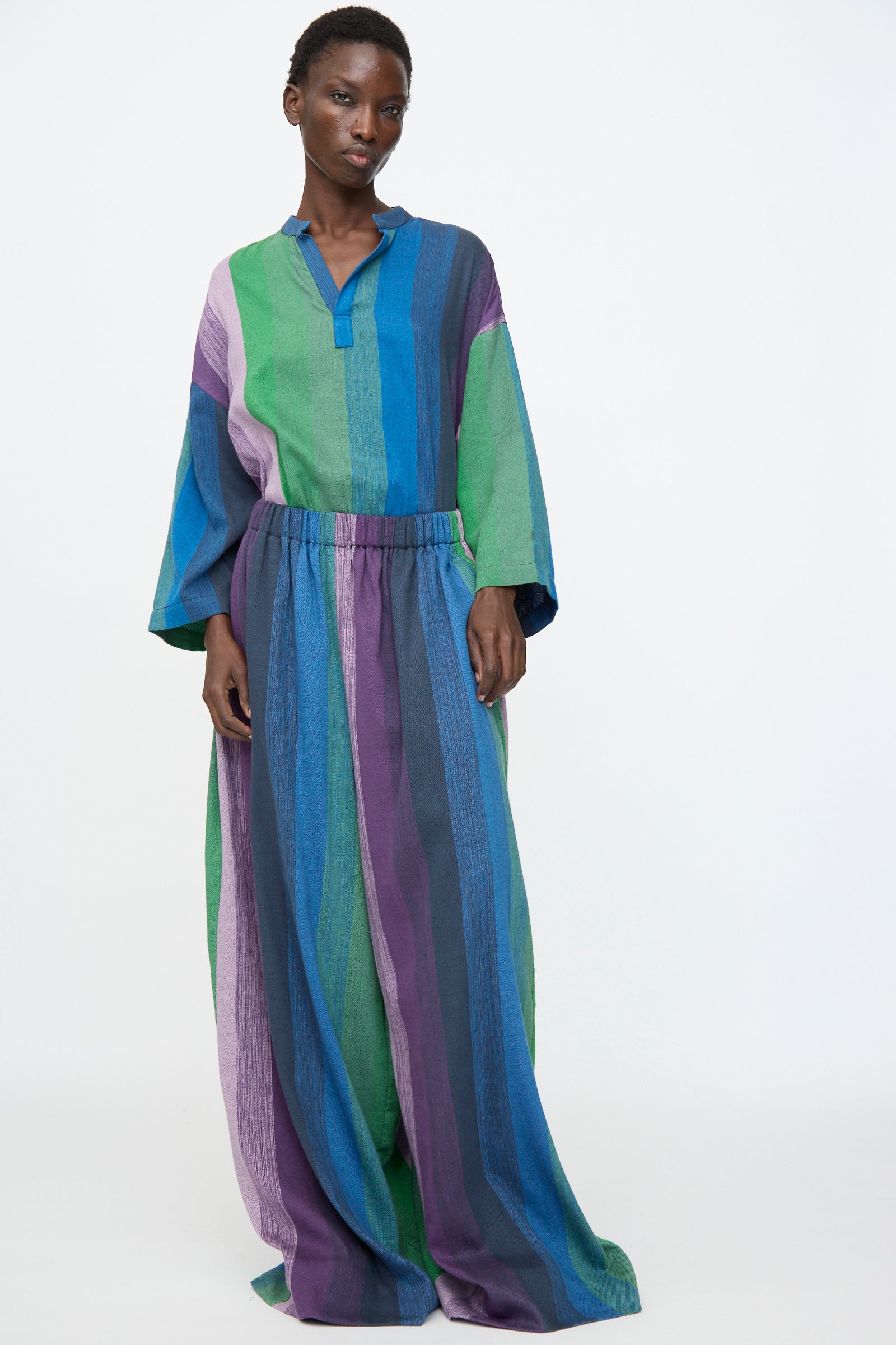 Person wearing the Marrakshi Life Wide Leg Pant in Stripe Multi, featuring blue, green, and purple stripes, standing against a plain white background.