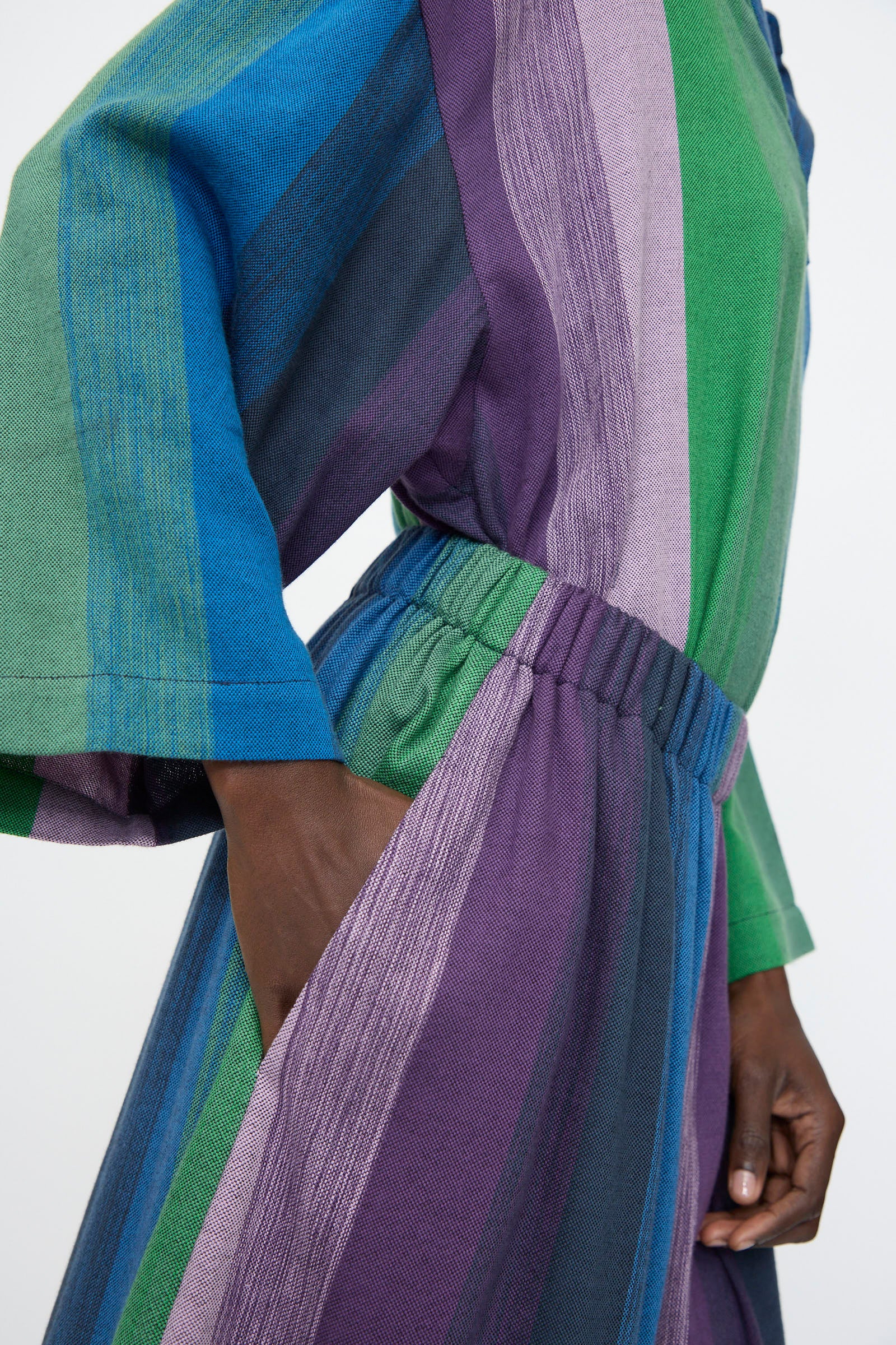 Person wearing Marrakshi Life’s Wide Leg Pant in Stripe Multi, featuring loose-fitting, striped cotton fabric in blue, green, and purple with an elasticated waist and side pocket for comfort.