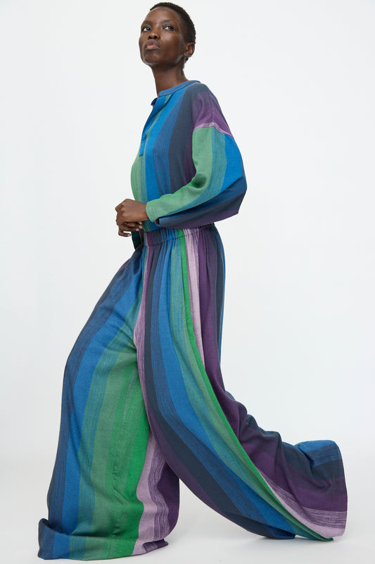 Model wears Marrakshi Life's Wide Leg Pant in Stripe Multi, featuring vertical green, blue, and purple stripes and an elasticated waist, styled with a loose-fit top against a plain white background.