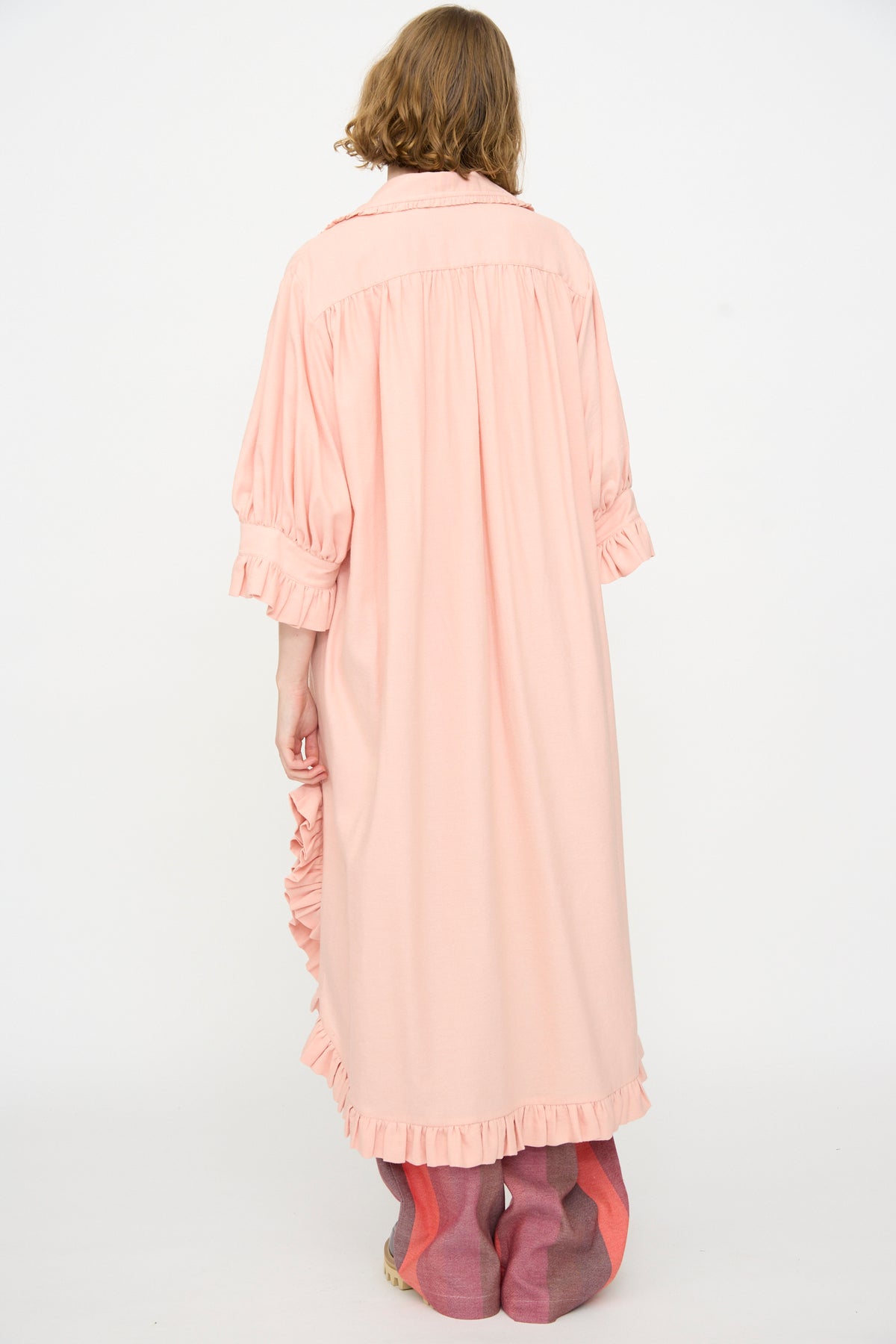 A person with shoulder-length hair is seen from behind wearing Marrakshi Life’s The Ruffled Tunic in Flesh—a loose, long-sleeved oversized dress with ruffles.