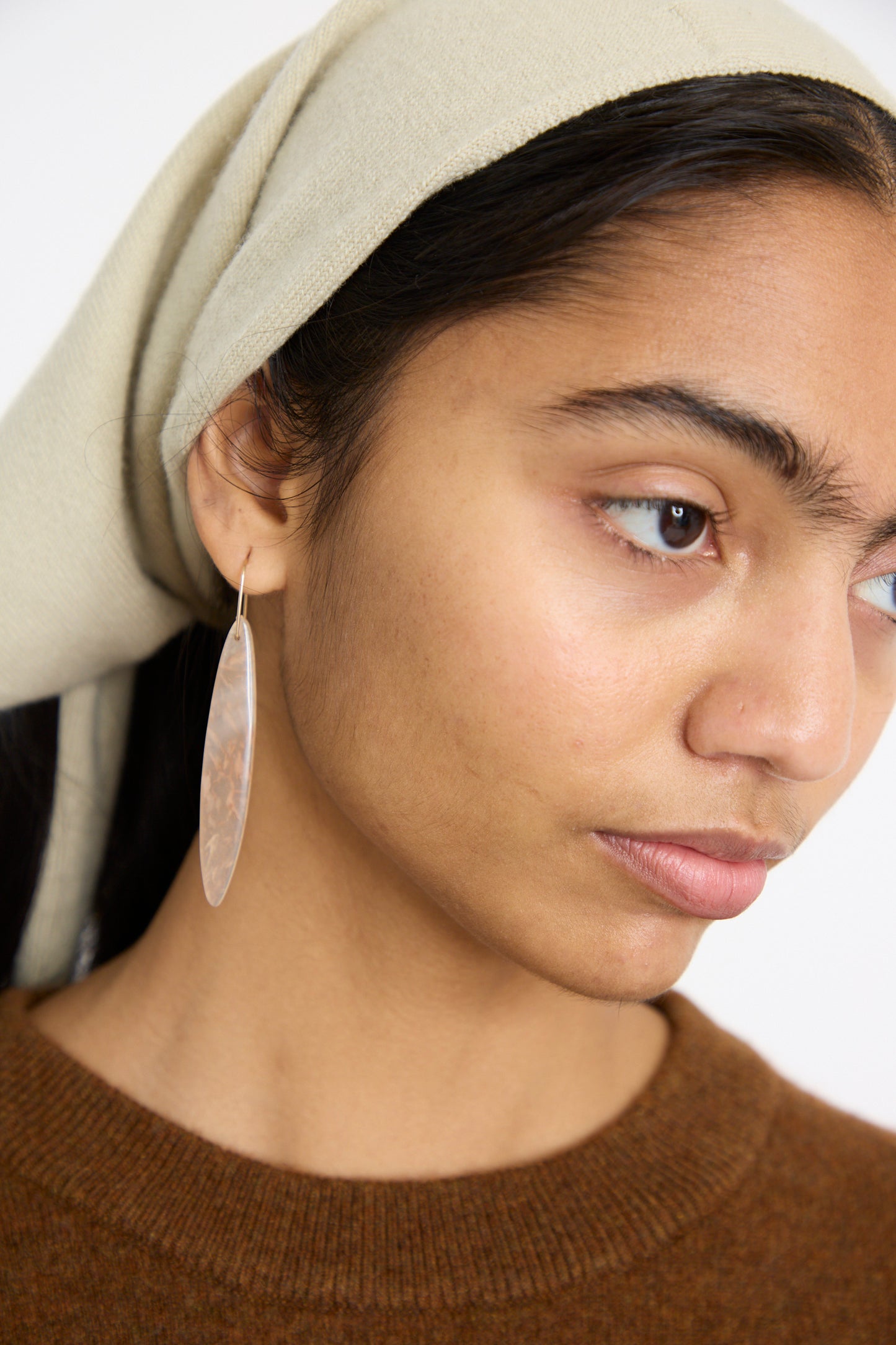 Against a plain background, a person in a beige headscarf and brown top gazes to the side, wearing Mary MacGill's Stone Drop Earrings in Cherry Agate.