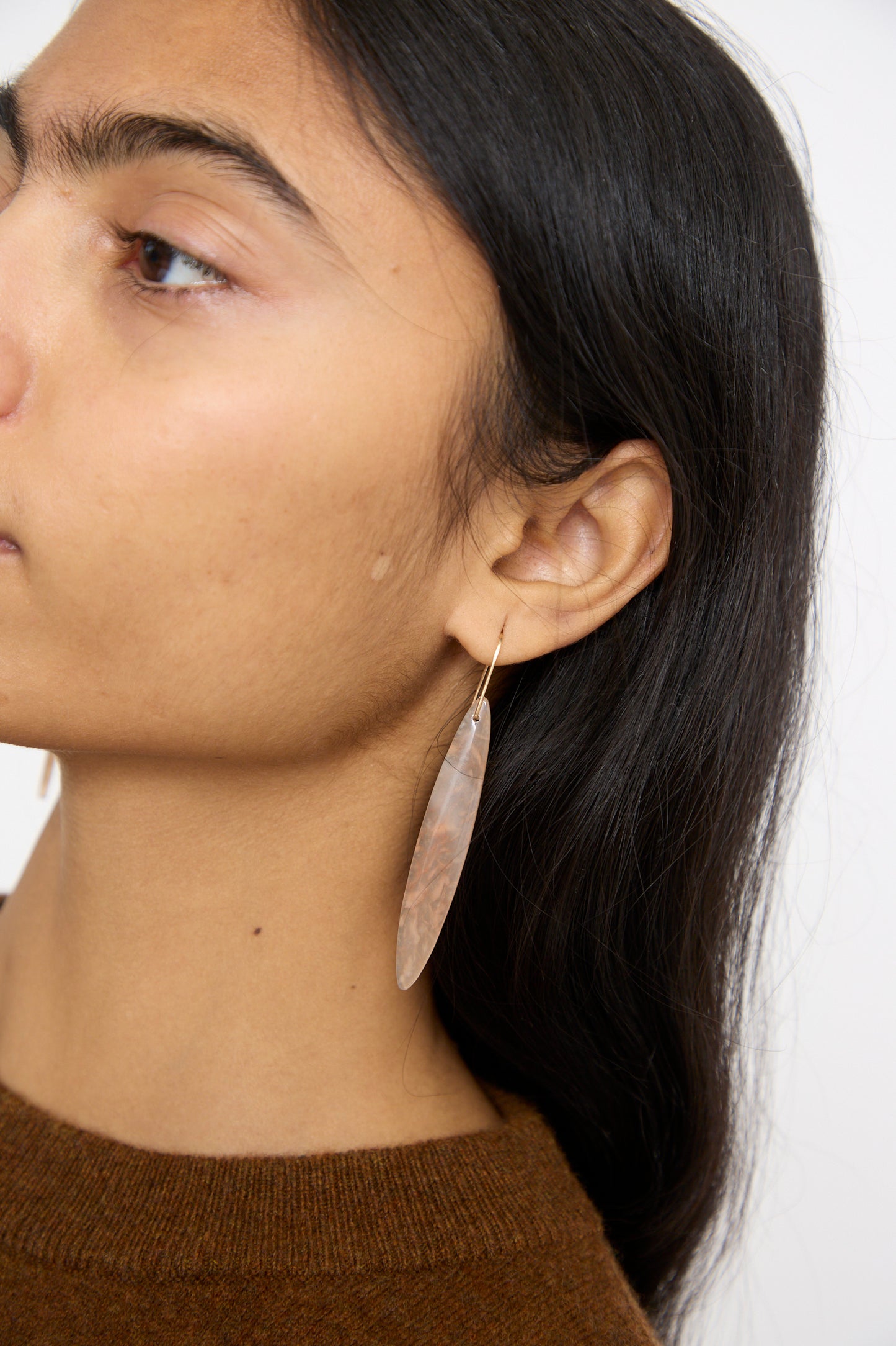 A person with long dark hair in a brown top showcases Mary MacGill's handmade Stone Drop Earrings in Cherry Agate, designed as large, elongated teardrops.