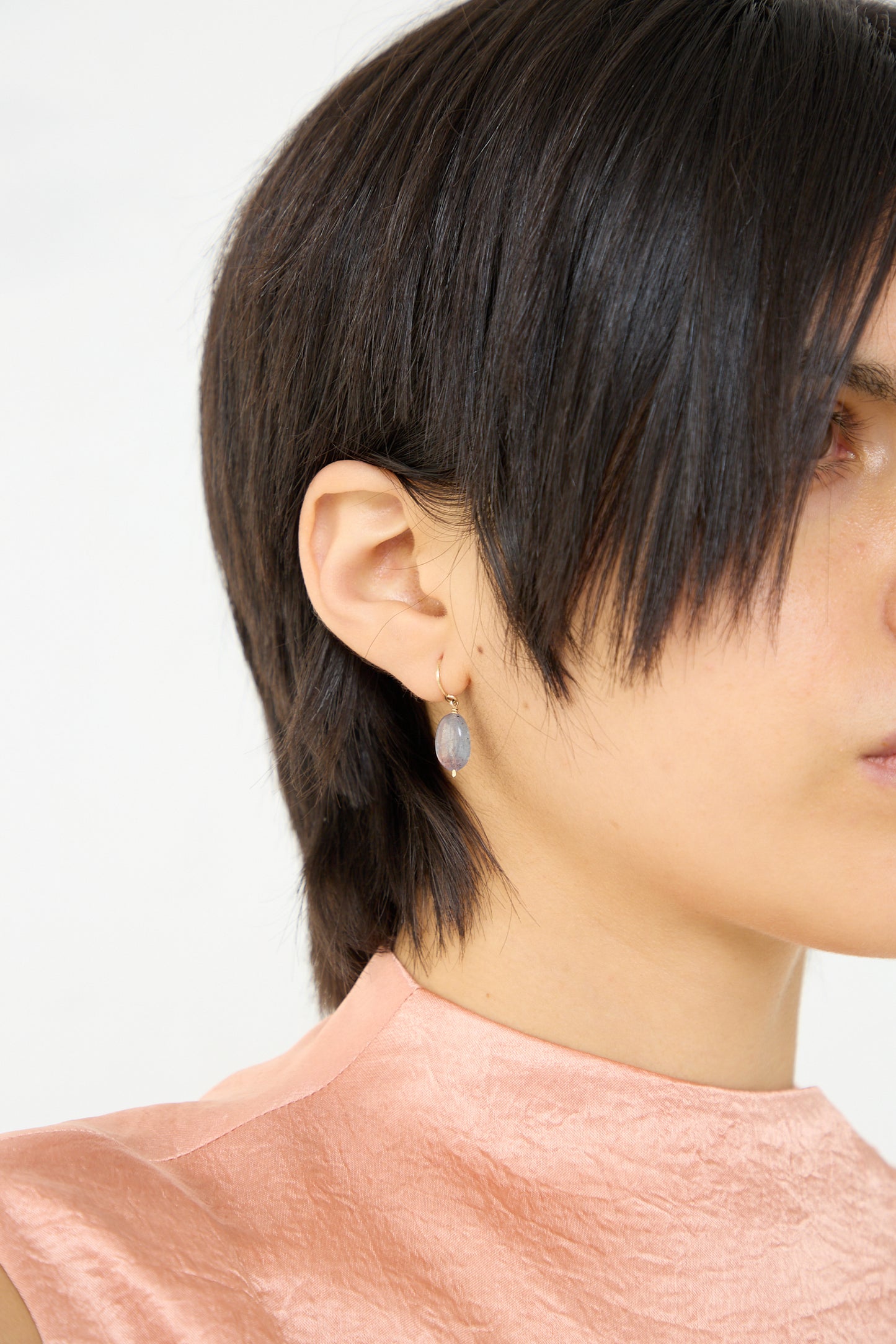 A woman wearing a pink top and Mary MacGill's 14K Crescent Charm Earrings in Iolite. Up close. Profile view.