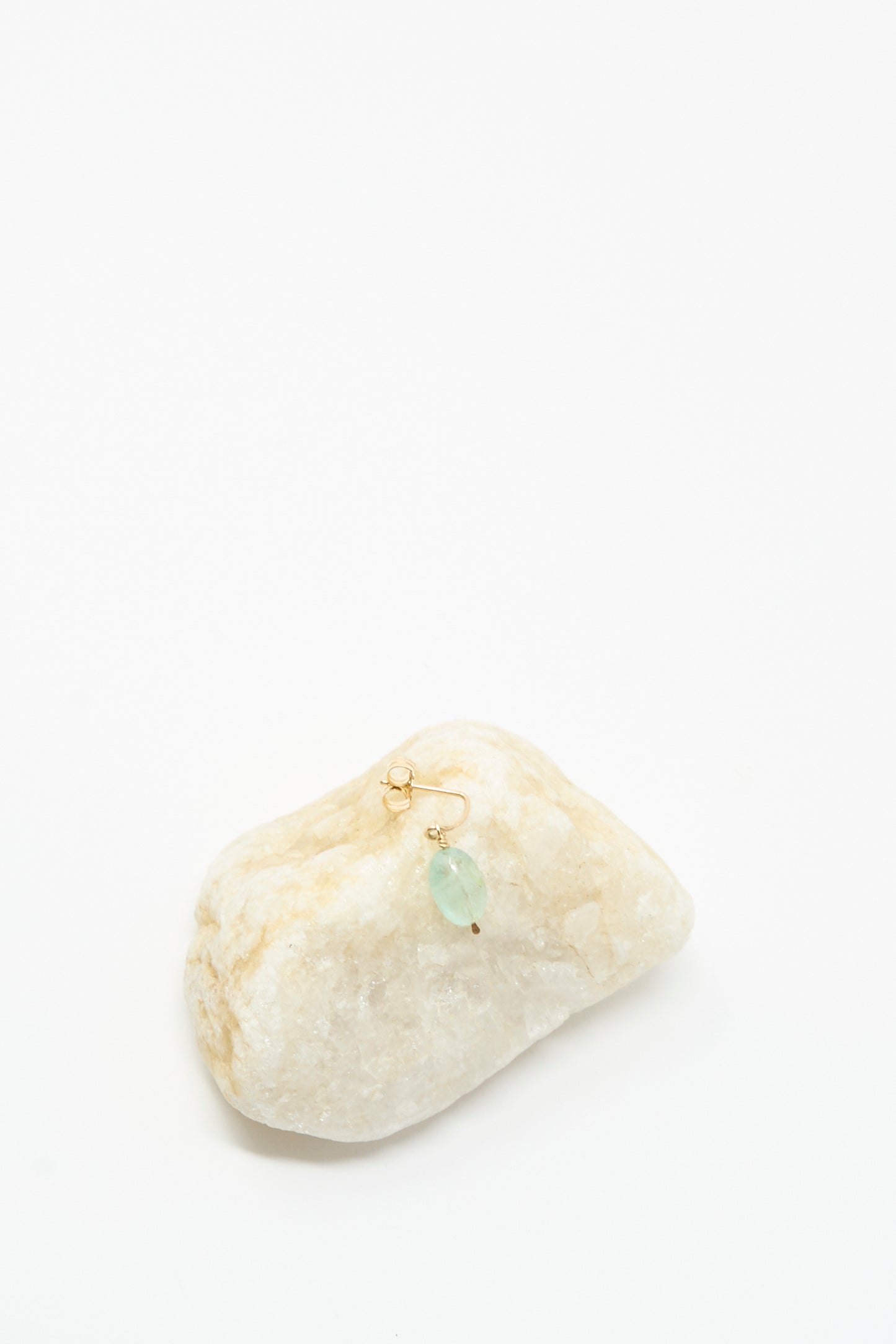 The Mary MacGill 14K Crescent Charm Single Earring in Aquamarine Stone is displayed on a white stone, with its gold hoop and translucent blue-green aquamarine bead set against a plain white background.