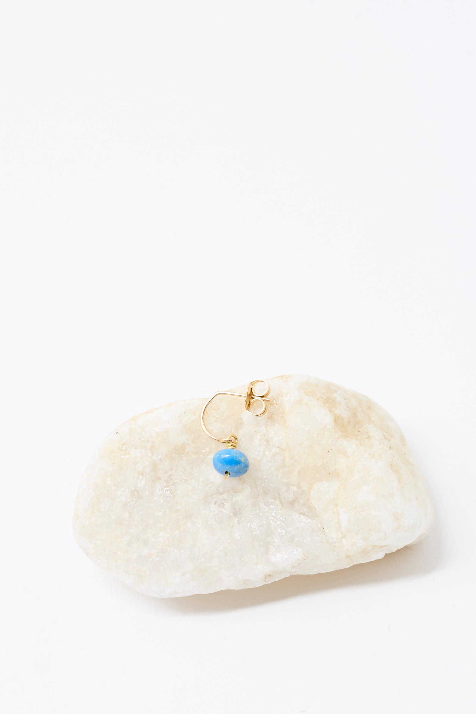 The Mary MacGill 14K Crescent Charm Single Earring in Ceruleite features a small blue bead and is shown on light-colored stone against a white background.