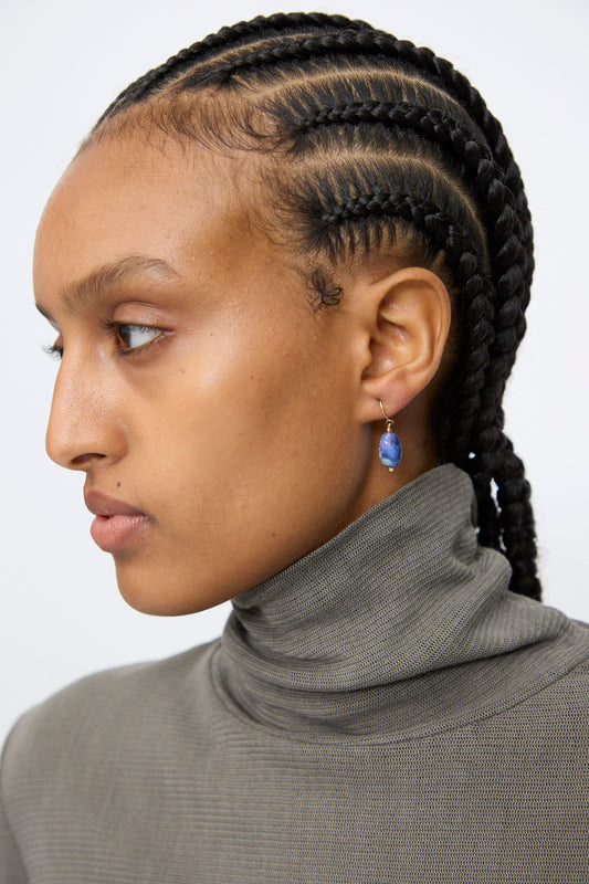 A person with braided hair wears a gray turtleneck and a Mary MacGill 14K Crescent Charm Single Earring in Dumortierite Quartz, shown in profile against a plain background.