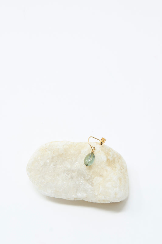 The Mary MacGill 14K Crescent Charm Single Earring in Round Tourmaline features a handmade gold design with a small green gemstone, shown dangling from a light-colored stone on a plain white background.