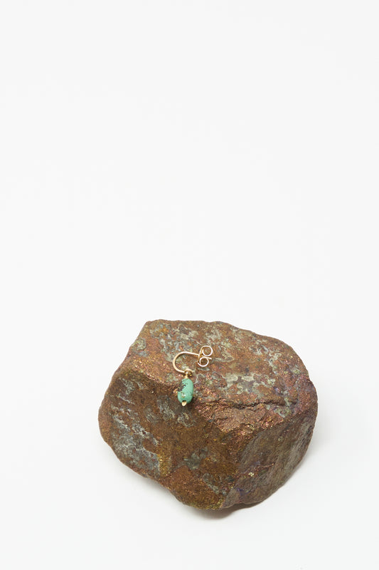 A single handmade Mary MacGill 14K Crescent Charm Earring in turquoise rests on a rough brown rock against a plain white background.