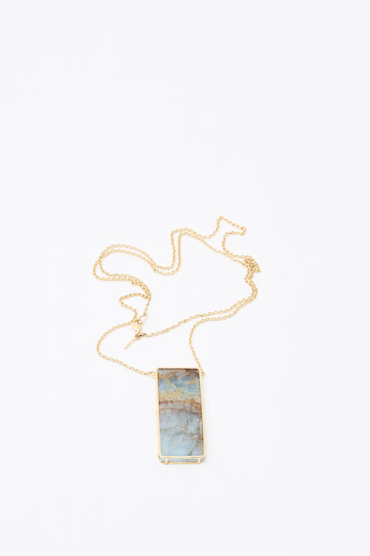 The Mary MacGill 14K Floating Necklace in Blue Calcite features a rectangular multicolored stone pendant on a gold chain, displayed against a white background—an elegant handmade jewelry piece.