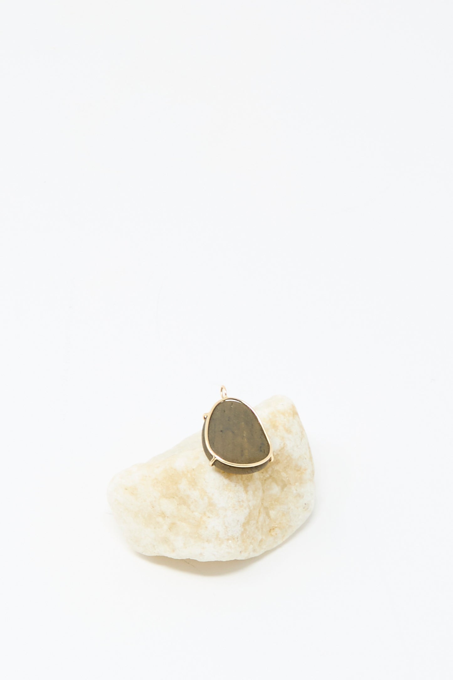 The Mary MacGill 14K Floating Pendant in Island Stone, featuring a handmade teardrop dark stone set in 14k gold, is displayed on a light rock against a white background.