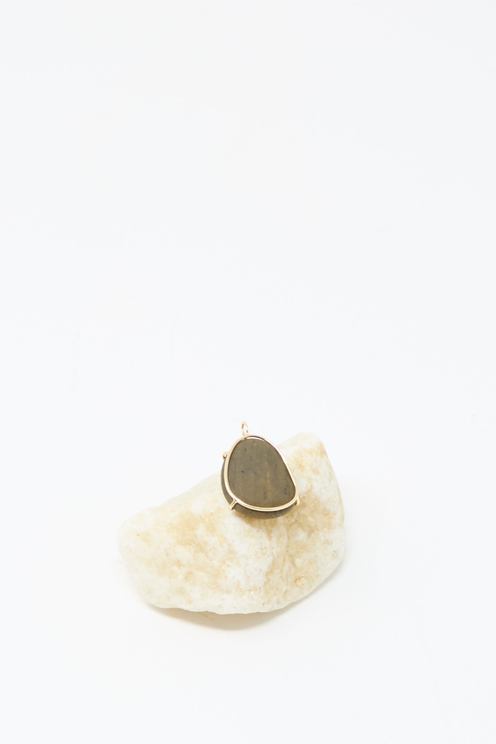 The Mary MacGill 14K Floating Pendant in Island Stone, featuring a handmade teardrop dark stone set in 14k gold, is displayed on a light rock against a white background.