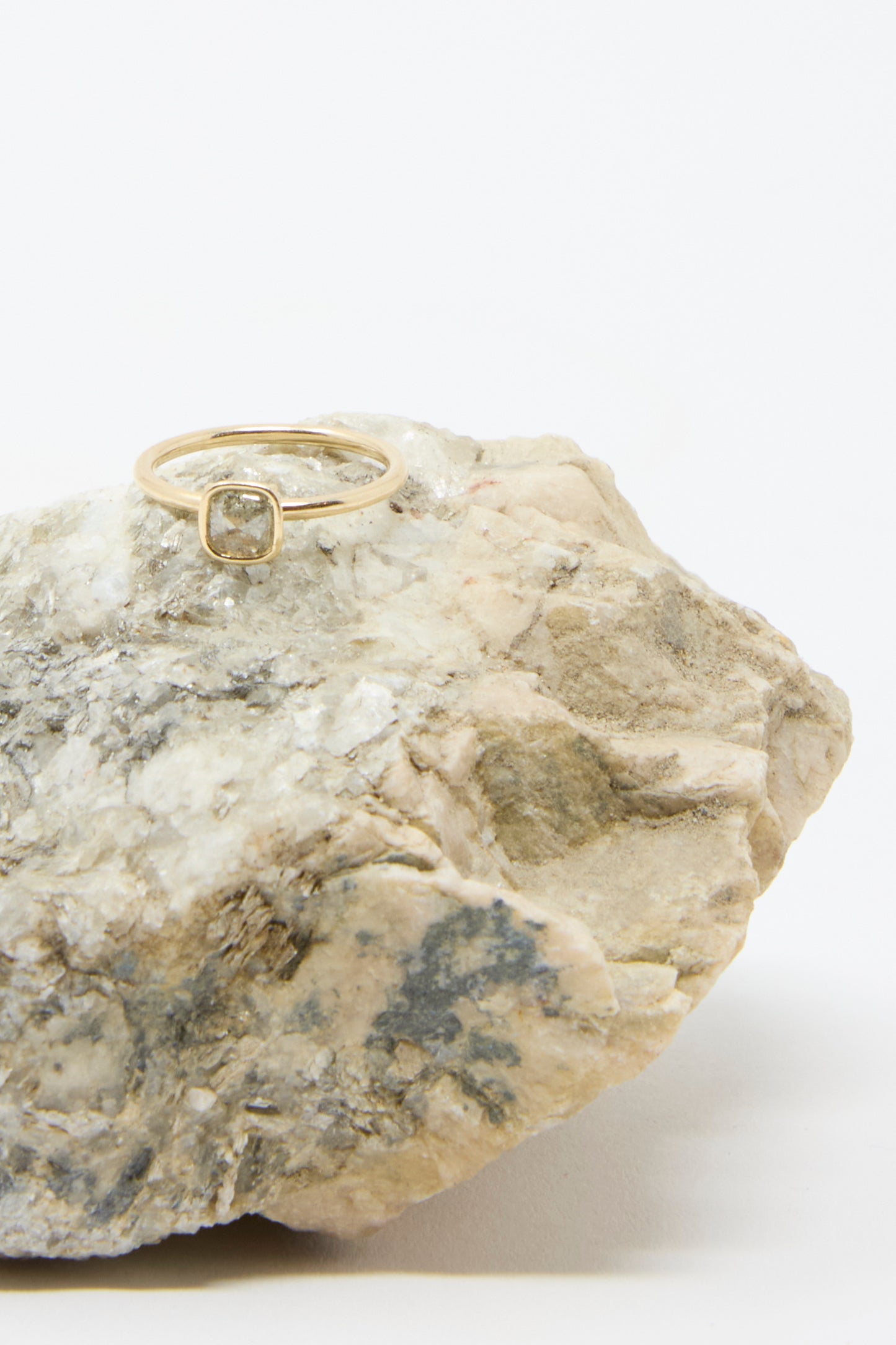 The 14K Floating Ring by Mary MacGill, featuring a salt and pepper rose cut mineral diamond, rests on a textured rock against a plain background.