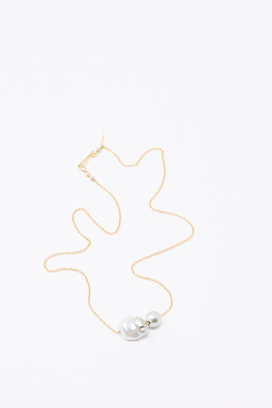 The 14K Mermaids Purse Necklace by Mary MacGill features Keshi and Tahitian pearls on a delicate gold chain, displayed elegantly on a white surface.