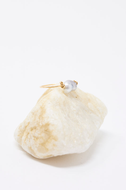 The Mary MacGill 14K Ring in Keshi Pearl—a handmade hammered gold ring with a single Keshi Pearl—rests on a light-colored stone against a white background.