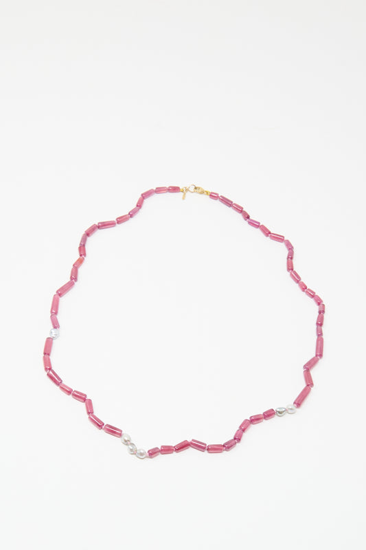 The Mary MacGill 14K Stone Layering Necklace features cylindrical ruby beads, small Keshi pearls, and a gold clasp, arranged in an elegant oval on a white background.