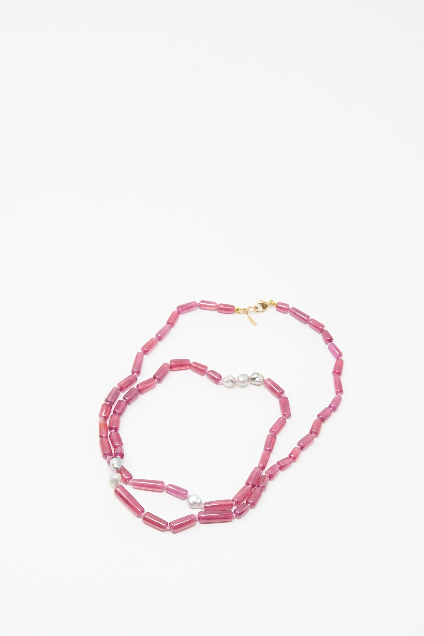 The Mary MacGill 14K Stone Layering Necklace features ruby and Keshi pearl stones with a gold clasp, arranged in a loose spiral on a white background.