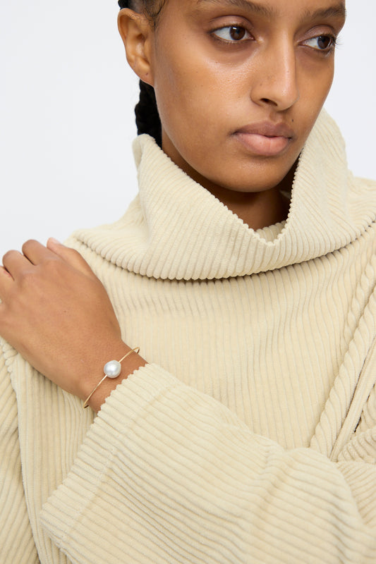 A person wearing a beige ribbed turtleneck sweater and the Mary MacGill 14K Tahitian Pearl Cuff in White on their wrist.