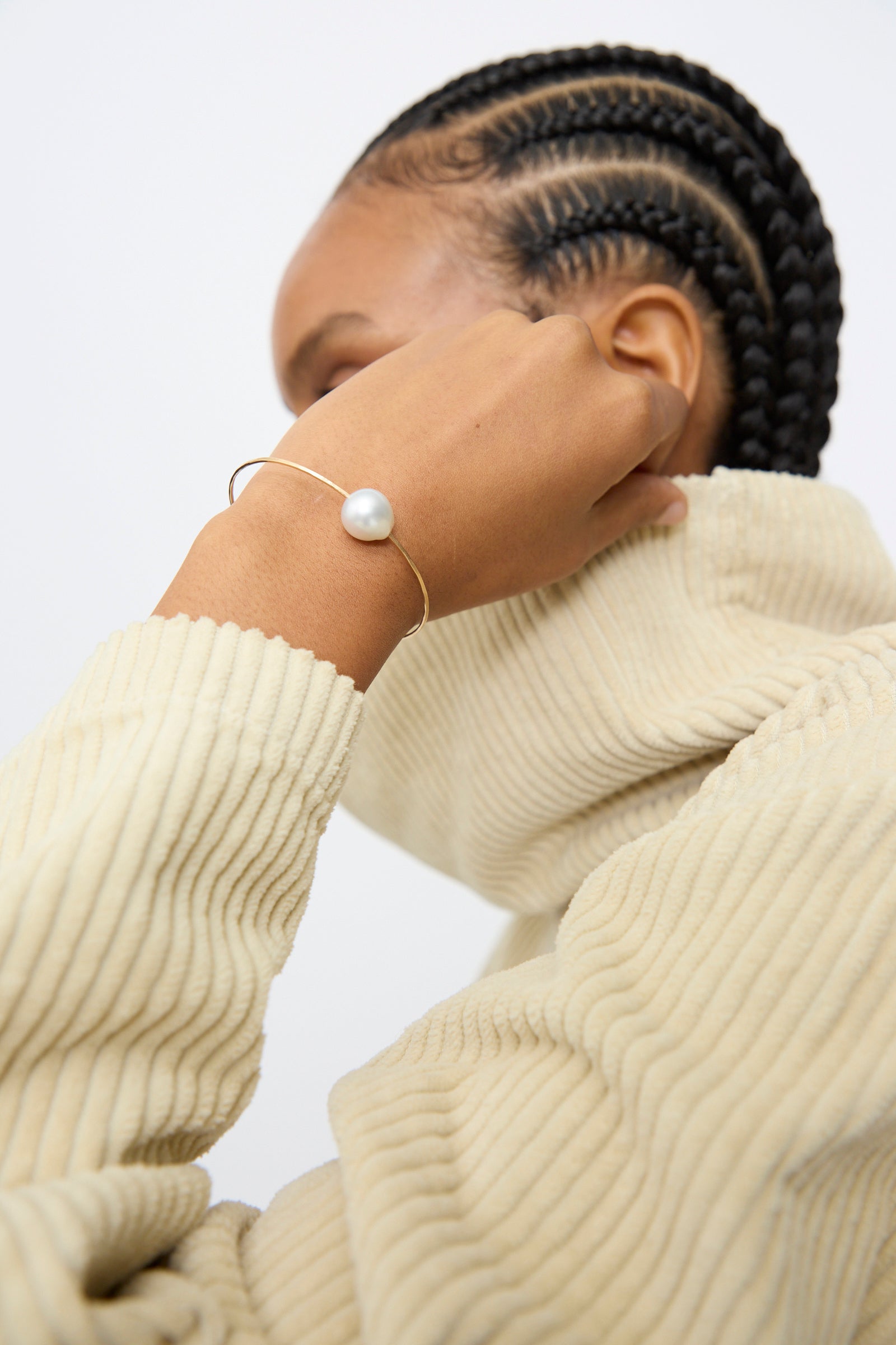 A person with cornrows, seen from behind, wears a light ribbed turtleneck and the Mary MacGill 14K Tahitian Pearl Cuff in White.