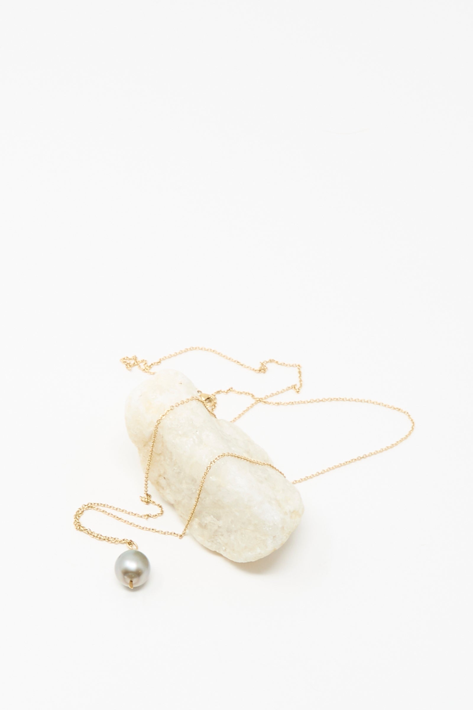 The Mary MacGill 14K Tahitian Pearl Drop Necklace in Charcoal Silver is displayed draped over a white stone against a plain white background.