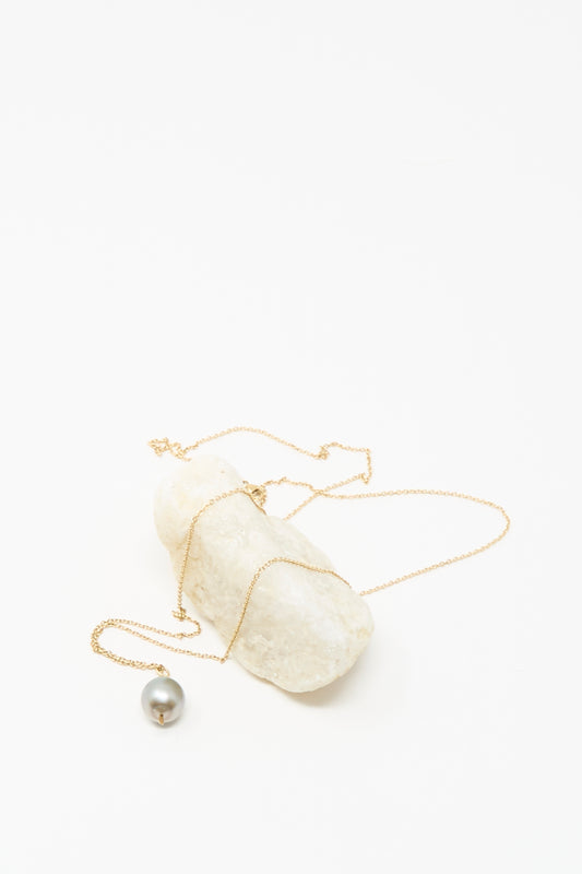 The Mary MacGill 14K Tahitian Pearl Drop Necklace in Charcoal Silver is displayed draped over a white stone against a plain white background.