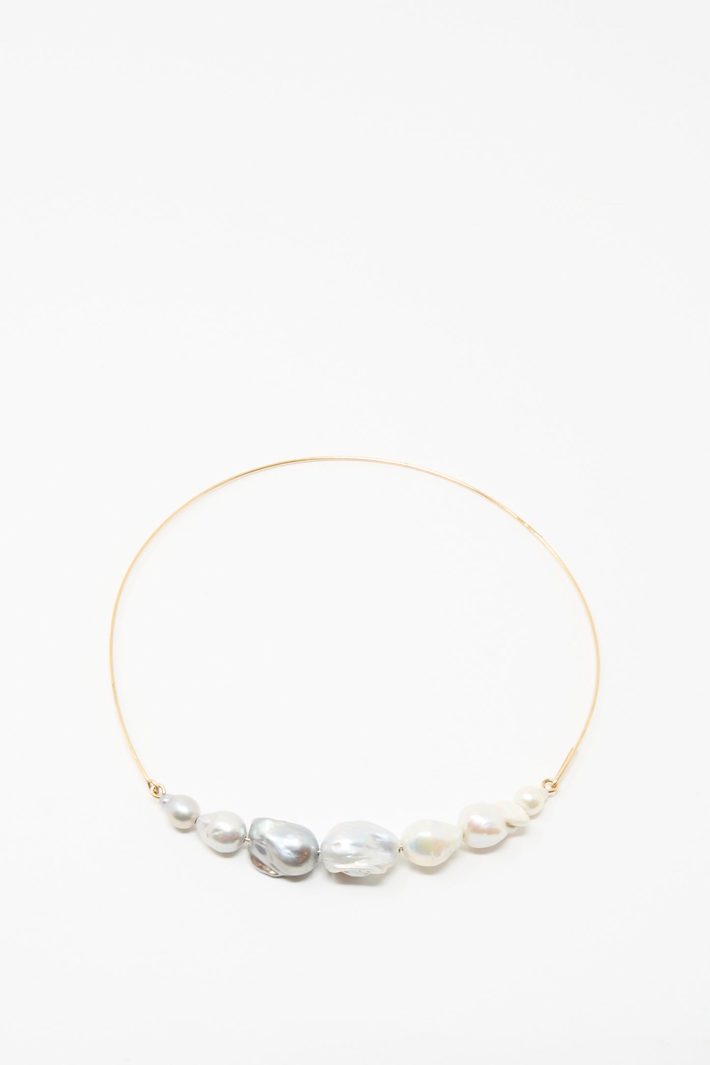 The Baroque Pearl Crescent Collar in Silver and White by Mary MacGill features seven handmade, uniquely shaped white and gray pearls arranged along a delicate silver choker.