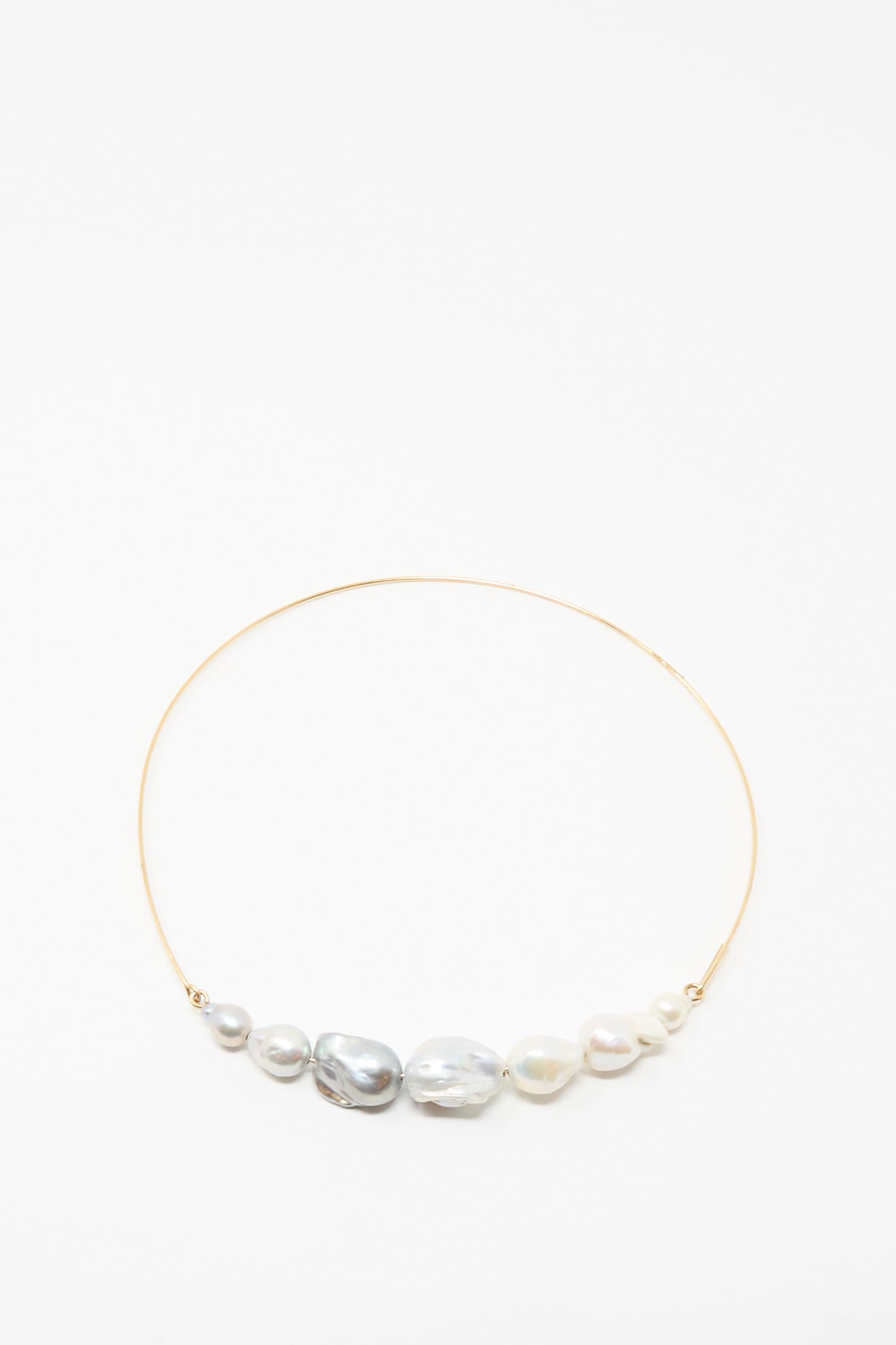The Baroque Pearl Crescent Collar in Silver and White by Mary MacGill features seven handmade, uniquely shaped white and gray pearls arranged along a delicate silver choker.