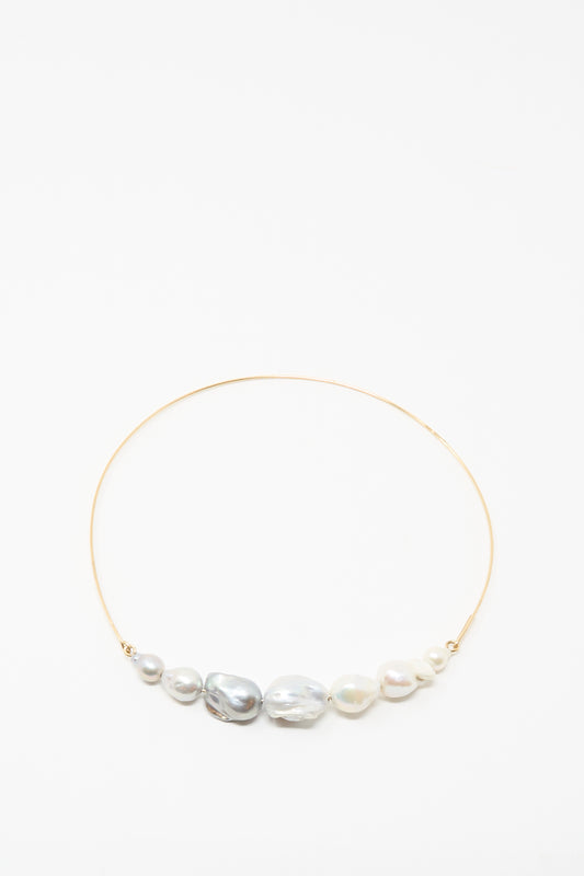 The Baroque Pearl Crescent Collar in Silver and White by Mary MacGill features seven handmade, uniquely shaped white and gray pearls arranged along a delicate silver choker.