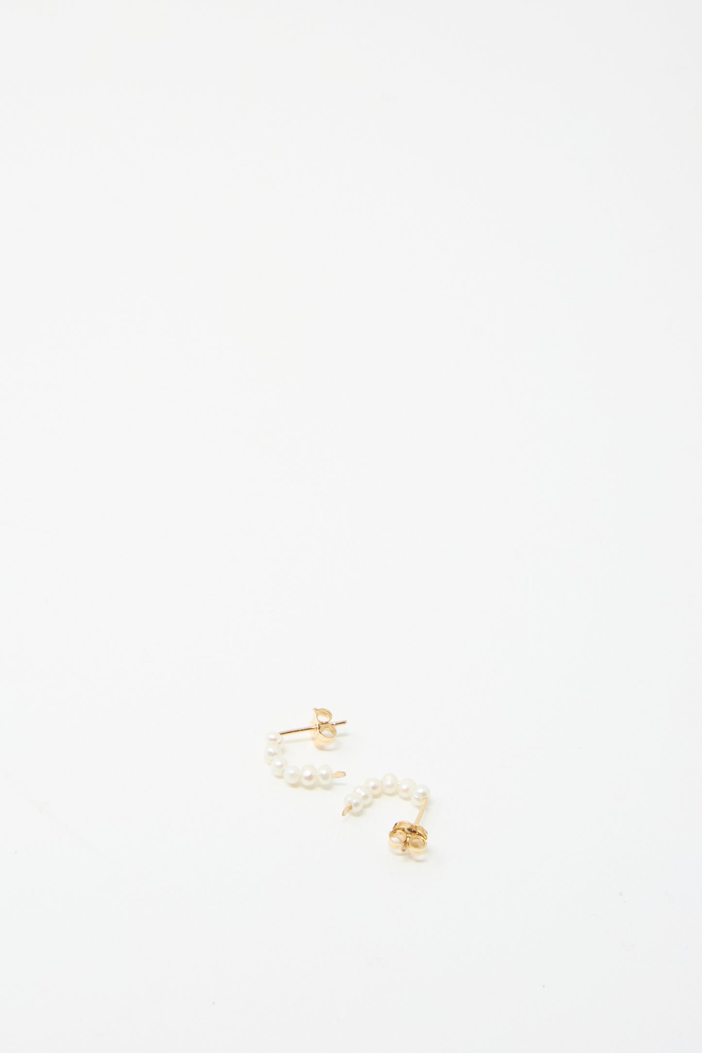 The Baroque Pearl Crescent Hoops by Mary MacGill feature baroque pearls hanging from gold-filled wire, forming handmade earrings set against a pristine white backdrop.