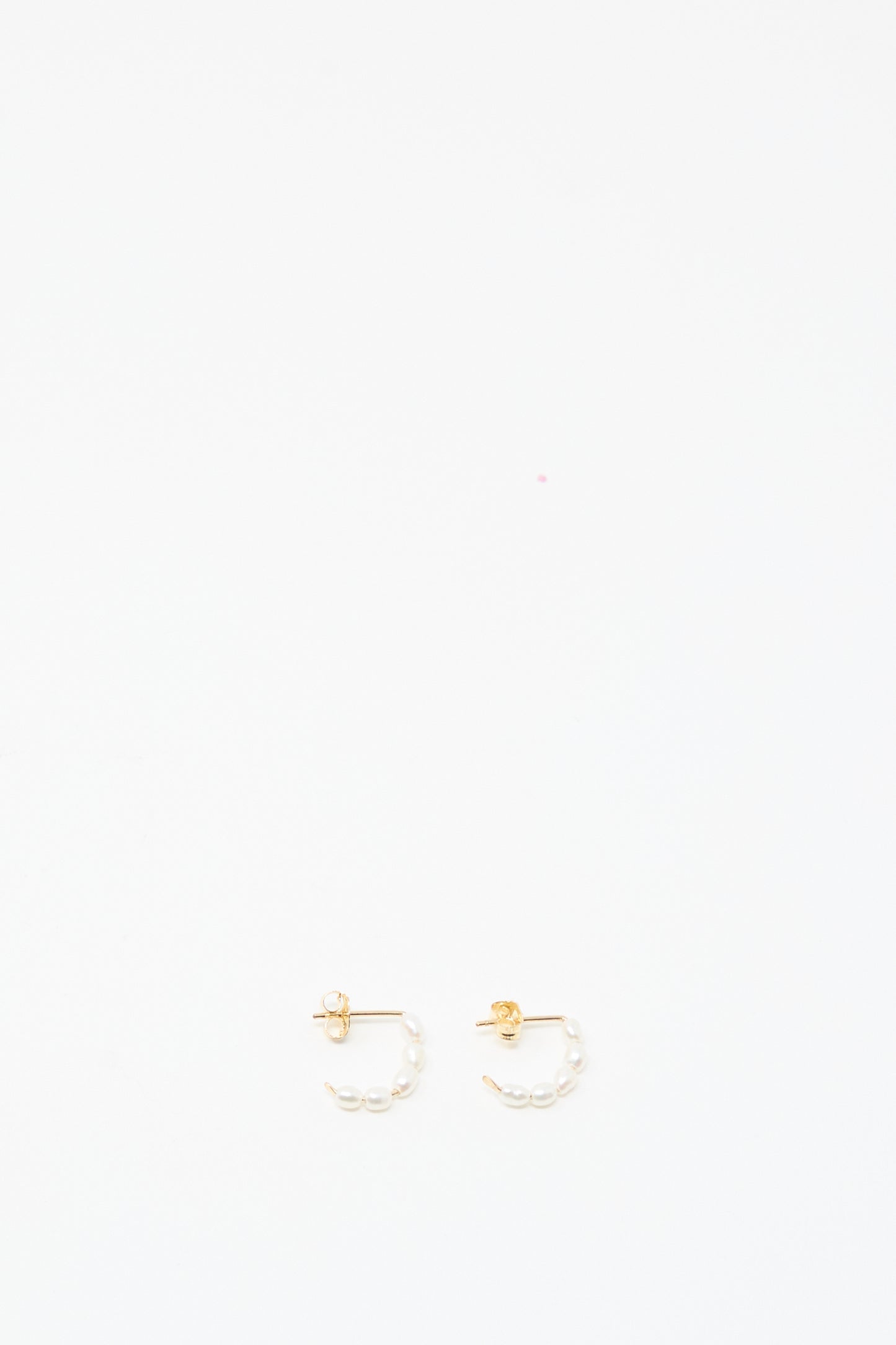 The Baroque Pearl Crescent Hoops by Mary MacGill are small handmade gold hoop earrings featuring white baroque pearl accents, shown on a plain white background.