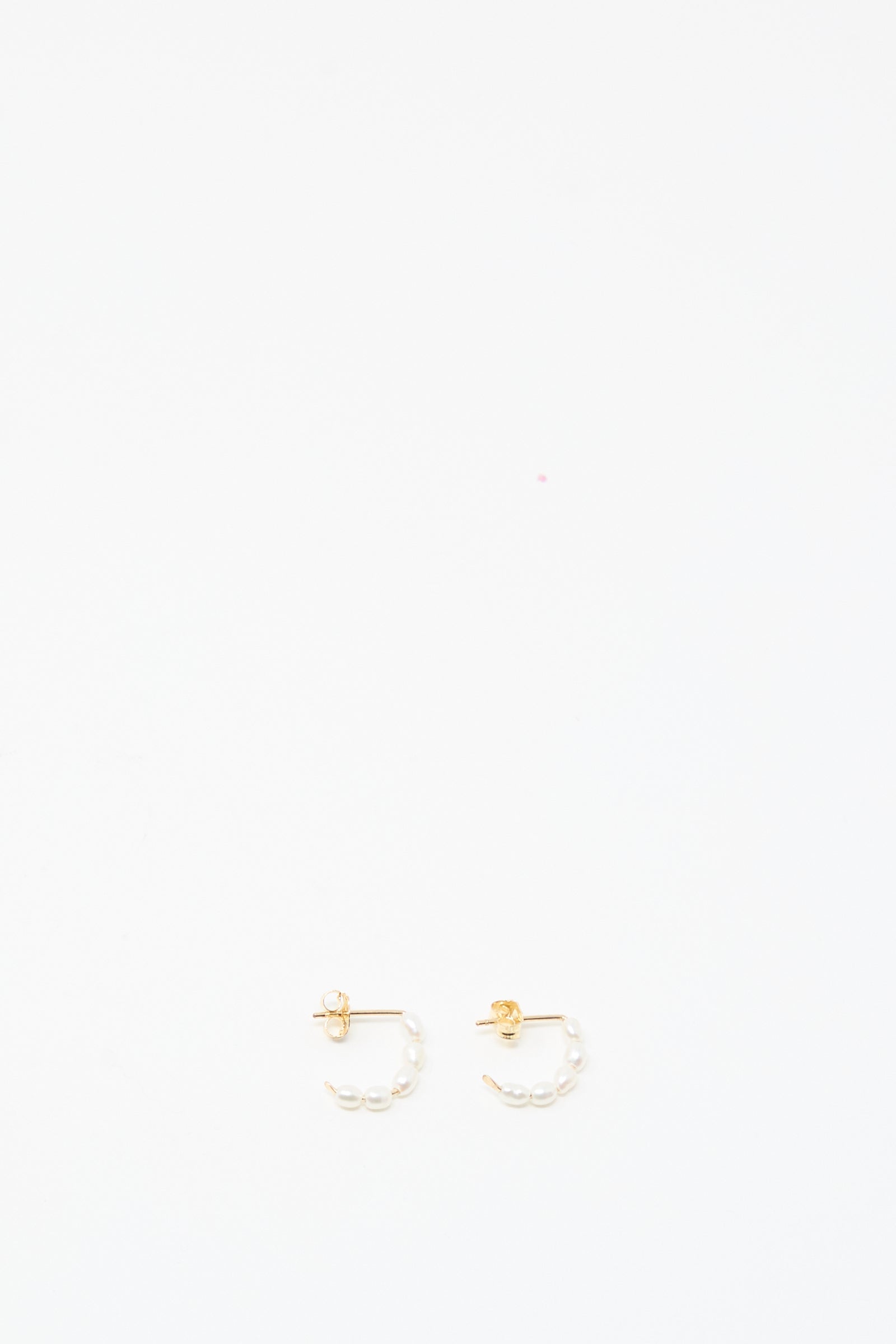 The Baroque Pearl Crescent Hoops by Mary MacGill are small handmade gold hoop earrings featuring white baroque pearl accents, shown on a plain white background.