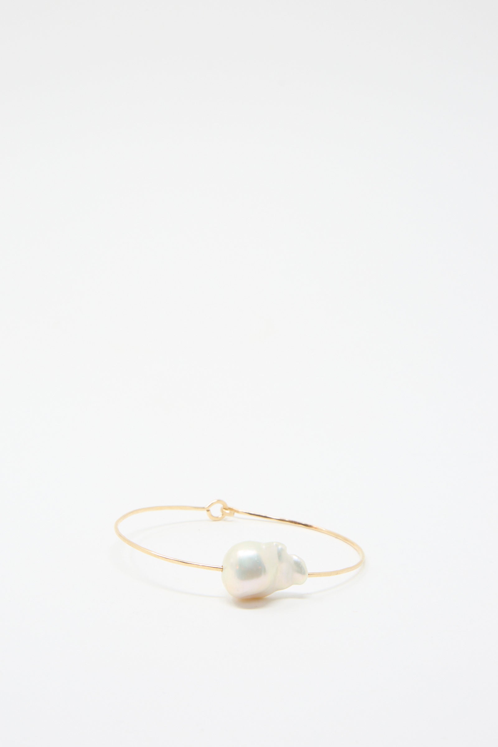 The Baroque Pearl Cuff Bracelet in White by Mary MacGill is a slender piece crafted from hammered gold-filled wire, showcasing a large, white Baroque pearl gracefully positioned at the front.