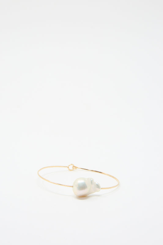 The Baroque Pearl Cuff Bracelet in White by Mary MacGill is a slender piece crafted from hammered gold-filled wire, showcasing a large, white Baroque pearl gracefully positioned at the front.