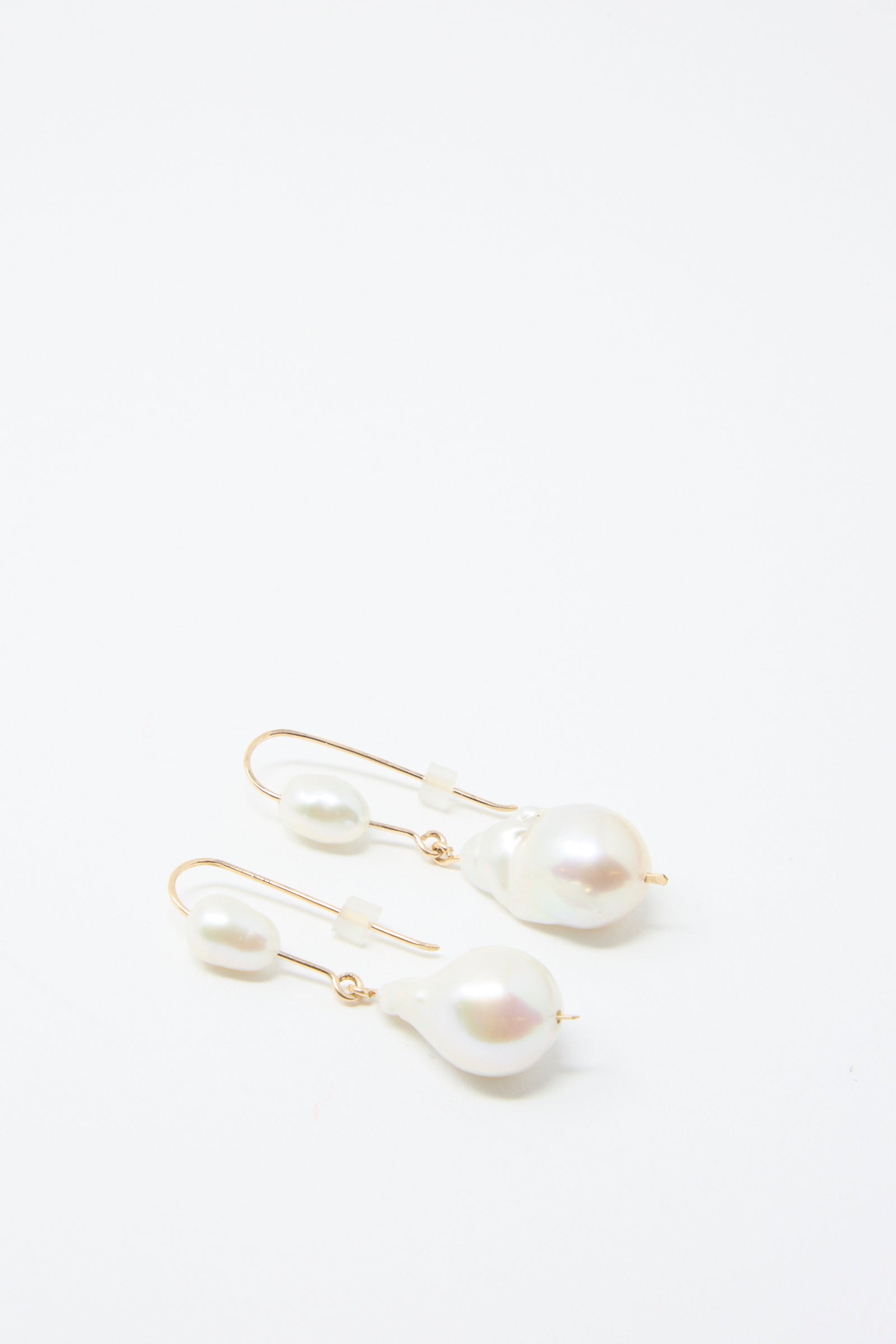 The Baroque Pearl Double Drop Earrings by Mary MacGill are exquisite pieces crafted with gold-filled wire, featuring white pearls and beads. These handmade earrings elegantly dangle against a pristine white background, embodying the charm of artisanal jewelry.