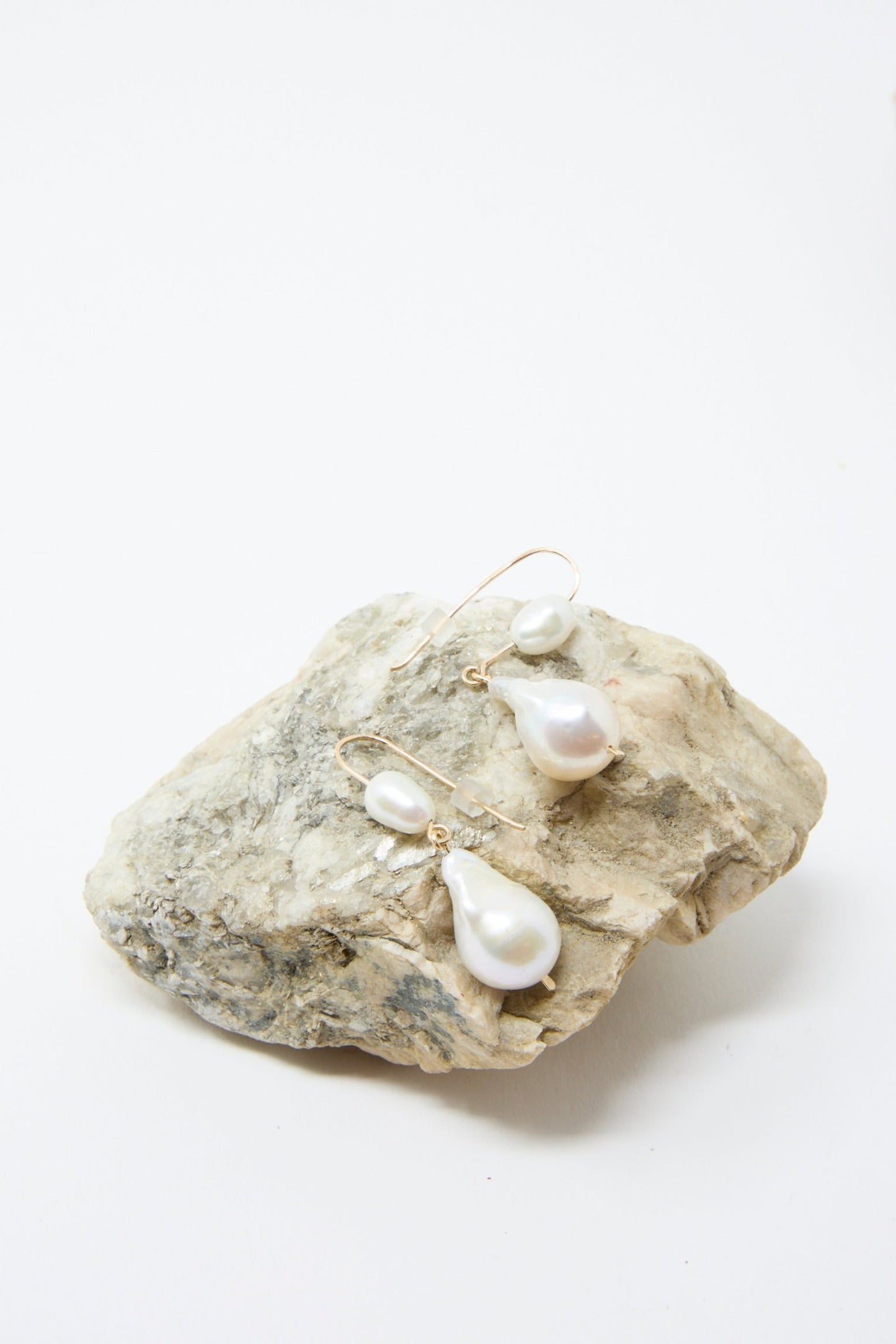 The exquisite Baroque Pearl Double Drop Earrings by Mary MacGill are elegantly displayed on a textured stone, their beauty accentuated by gold-filled wire, set against a plain white background.