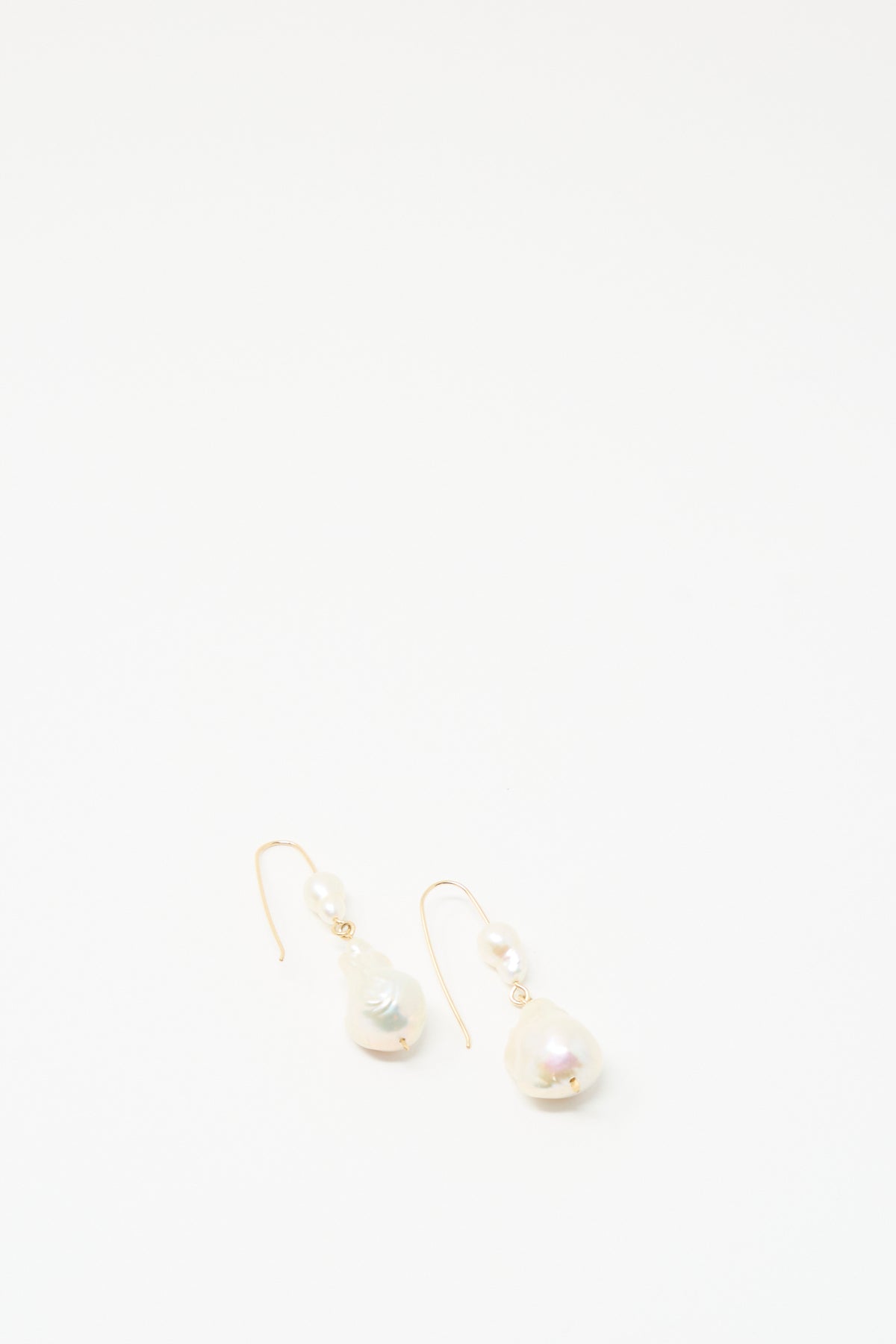 The Baroque Pearl Double Drop Earrings in White by Mary MacGill, featuring white pearls, rest on a plain white background.