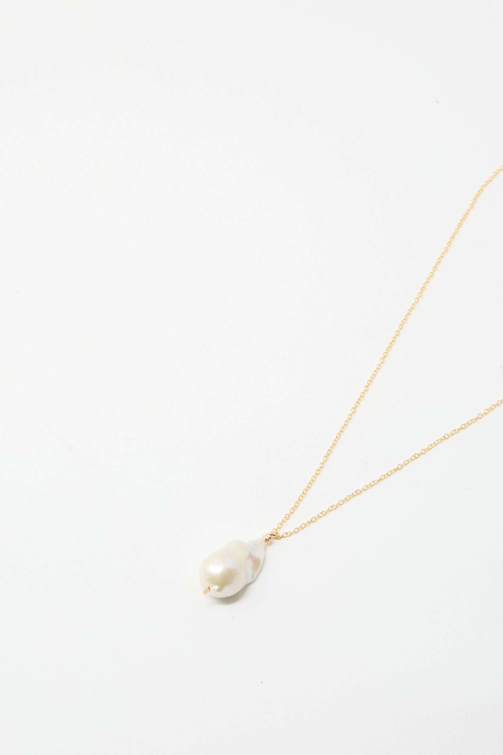 Introducing the Baroque Pearl Drop Necklace in White by Mary MacGill—a unique handmade piece featuring a gold chain with a striking large baroque pearl pendant, showcased against a plain white background.