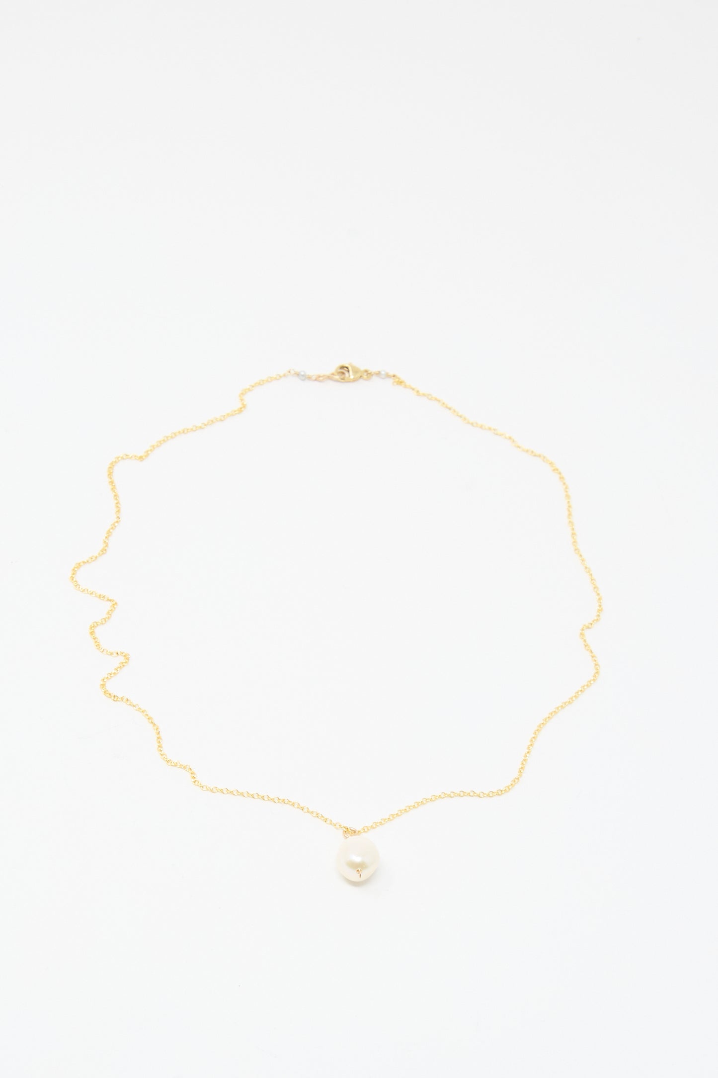 The Mary MacGill Baroque Pearl Drop Necklace in White - 18" is a handmade gold chain with a single round baroque pearl pendant, shown on a white background.