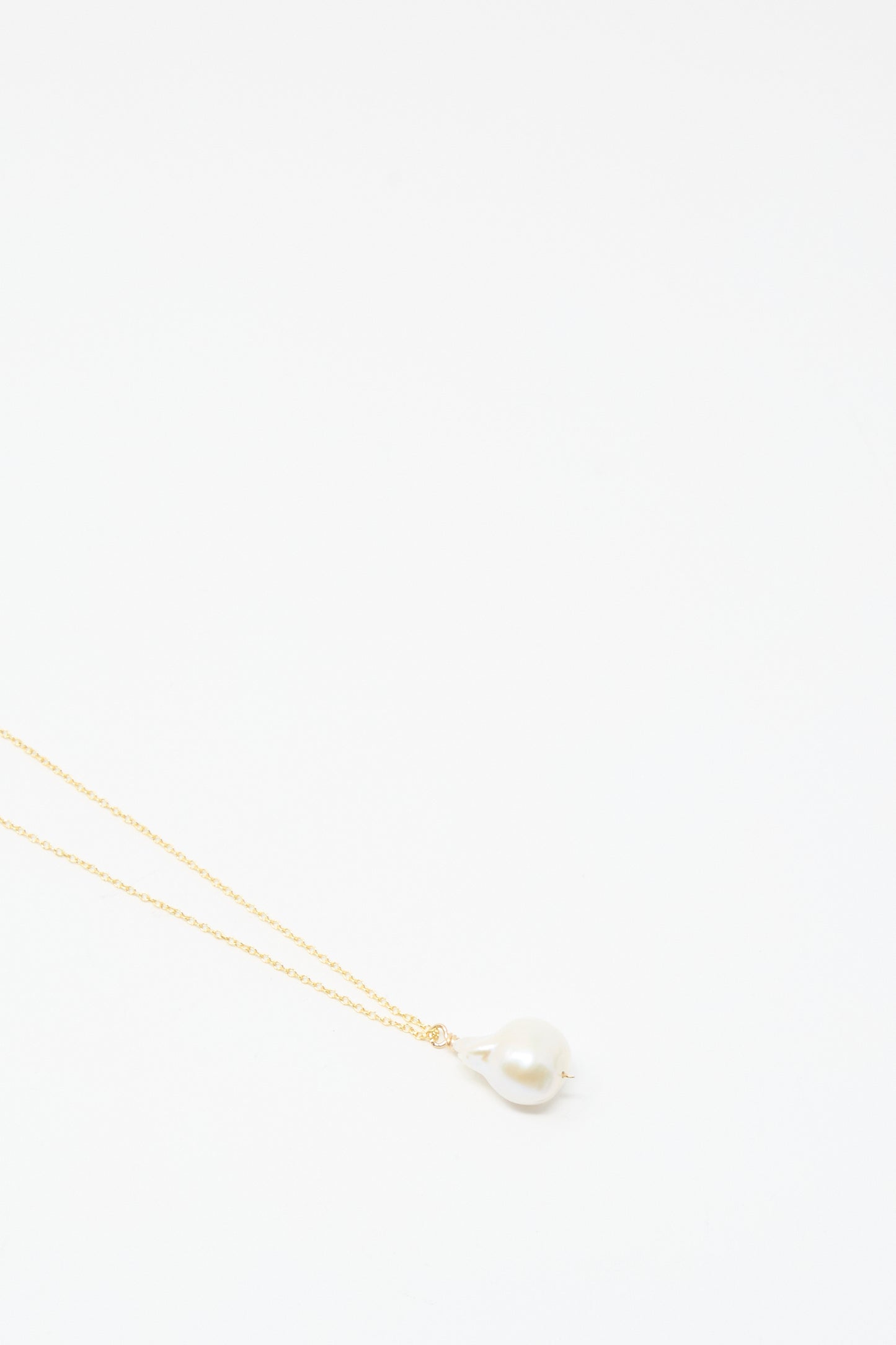 The Mary MacGill Baroque Pearl Drop Necklace in White, 28", features a handmade gold chain with a single baroque pearl pendant, elegantly displayed against a plain white background.
