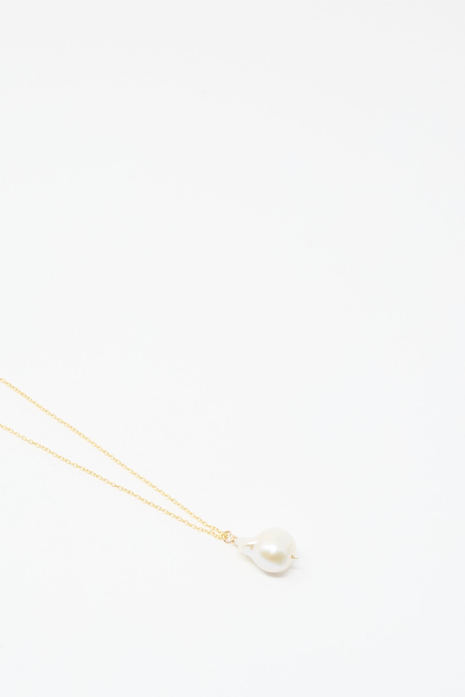 The Mary MacGill Baroque Pearl Drop Necklace in White, 28", features a handmade gold chain with a single baroque pearl pendant, elegantly displayed against a plain white background.