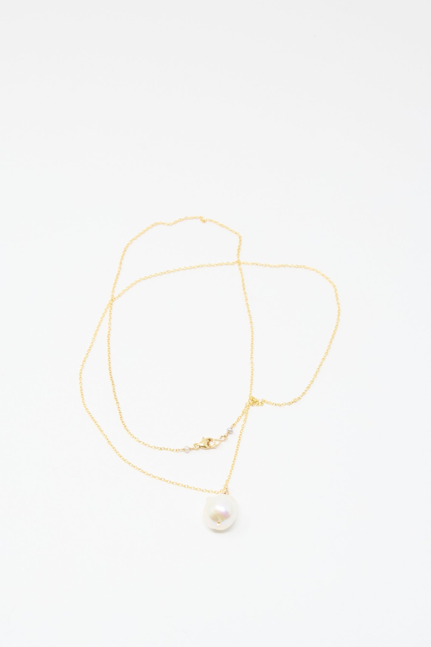 The Mary MacGill Baroque Pearl Drop Necklace in White (28") is a delicate handmade gold chain with a single round white pearl pendant, echoing classic baroque style, shown on a plain white background.