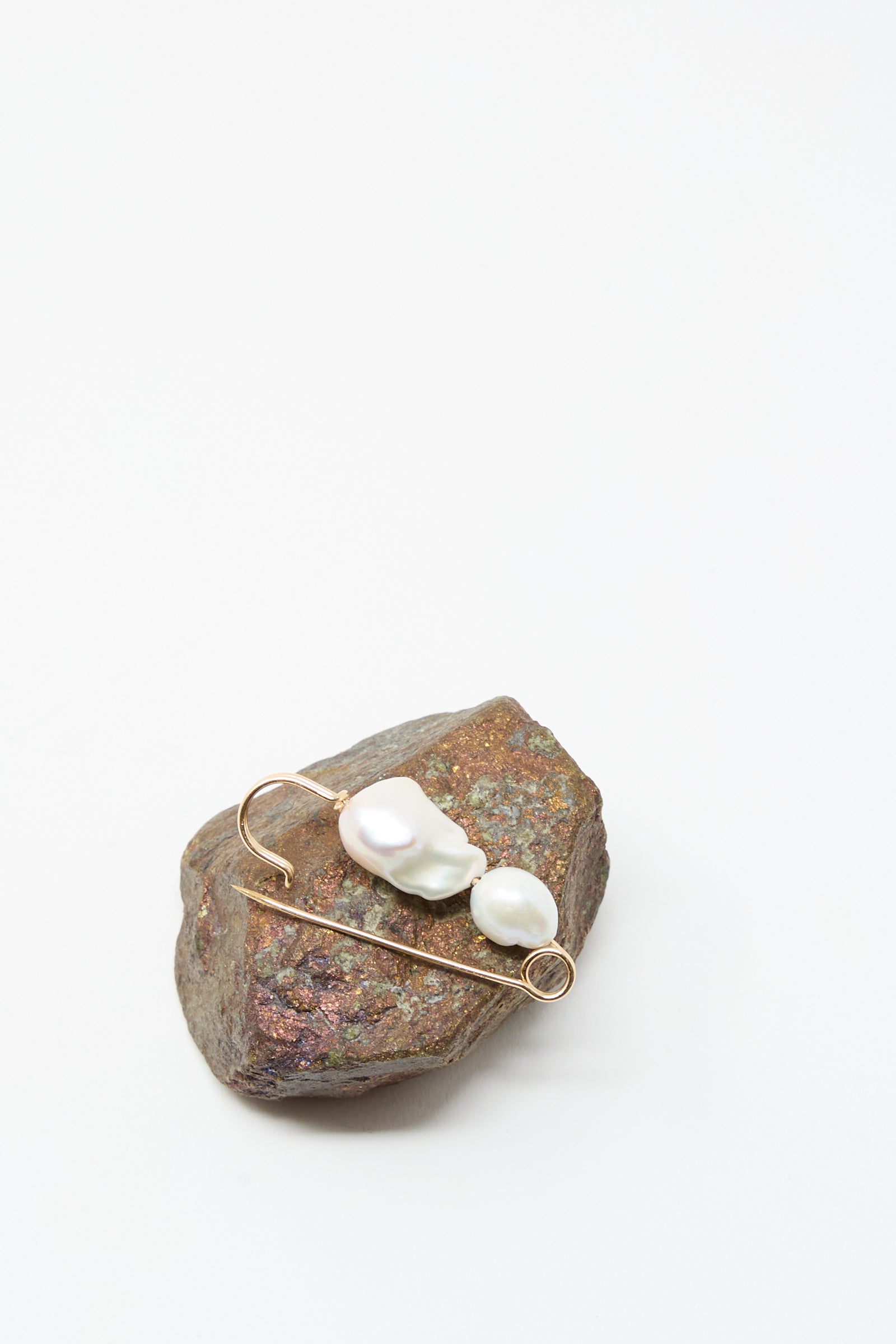 The Mary MacGill Baroque Pearl Pin in White is shown on a rough brown stone with a white background.