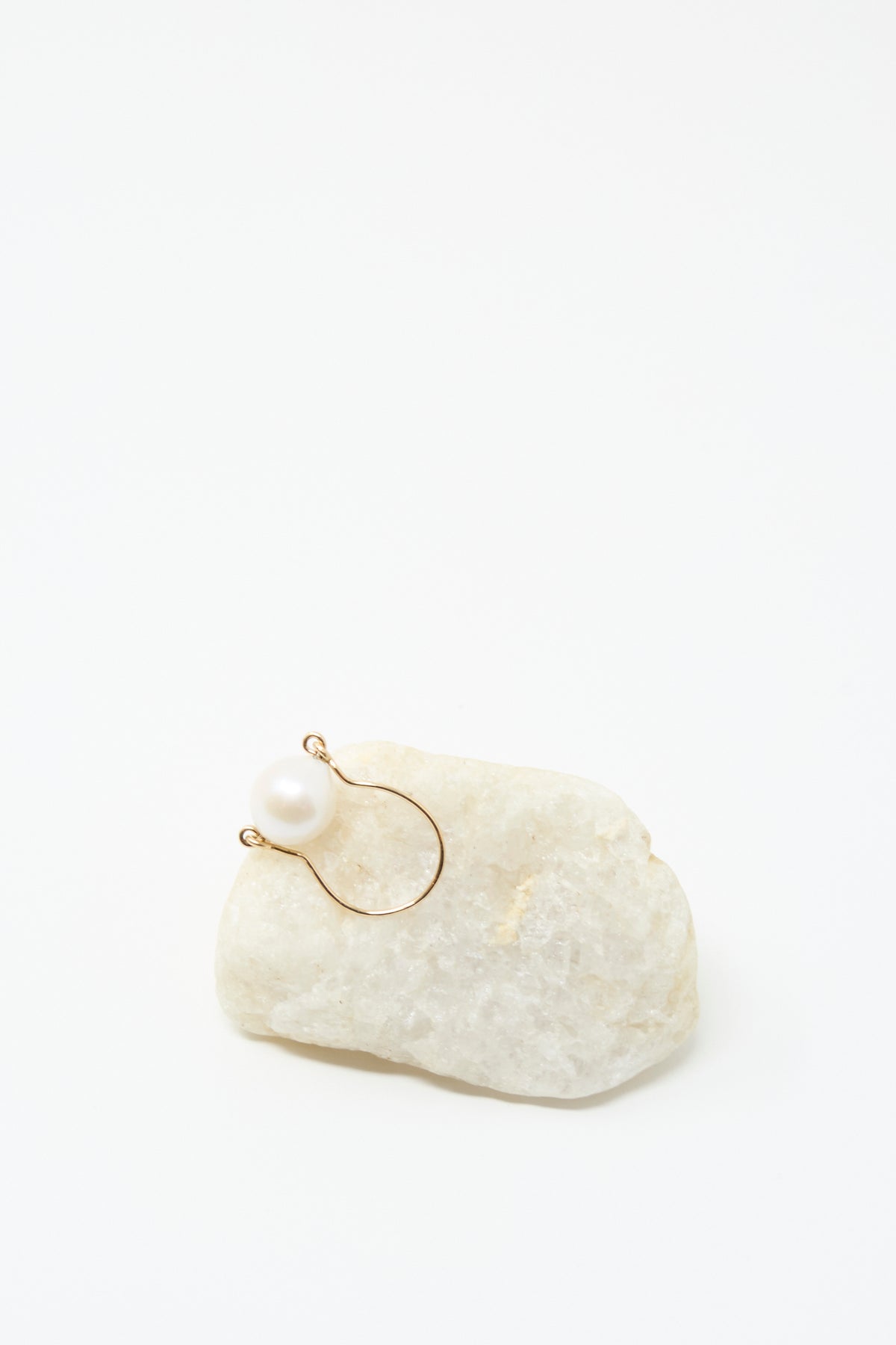 The Baroque Pearl Ring in White by Mary MacGill, crafted from gold-filled wire and a white pearl, is displayed on an off-white stone with a plain white background.