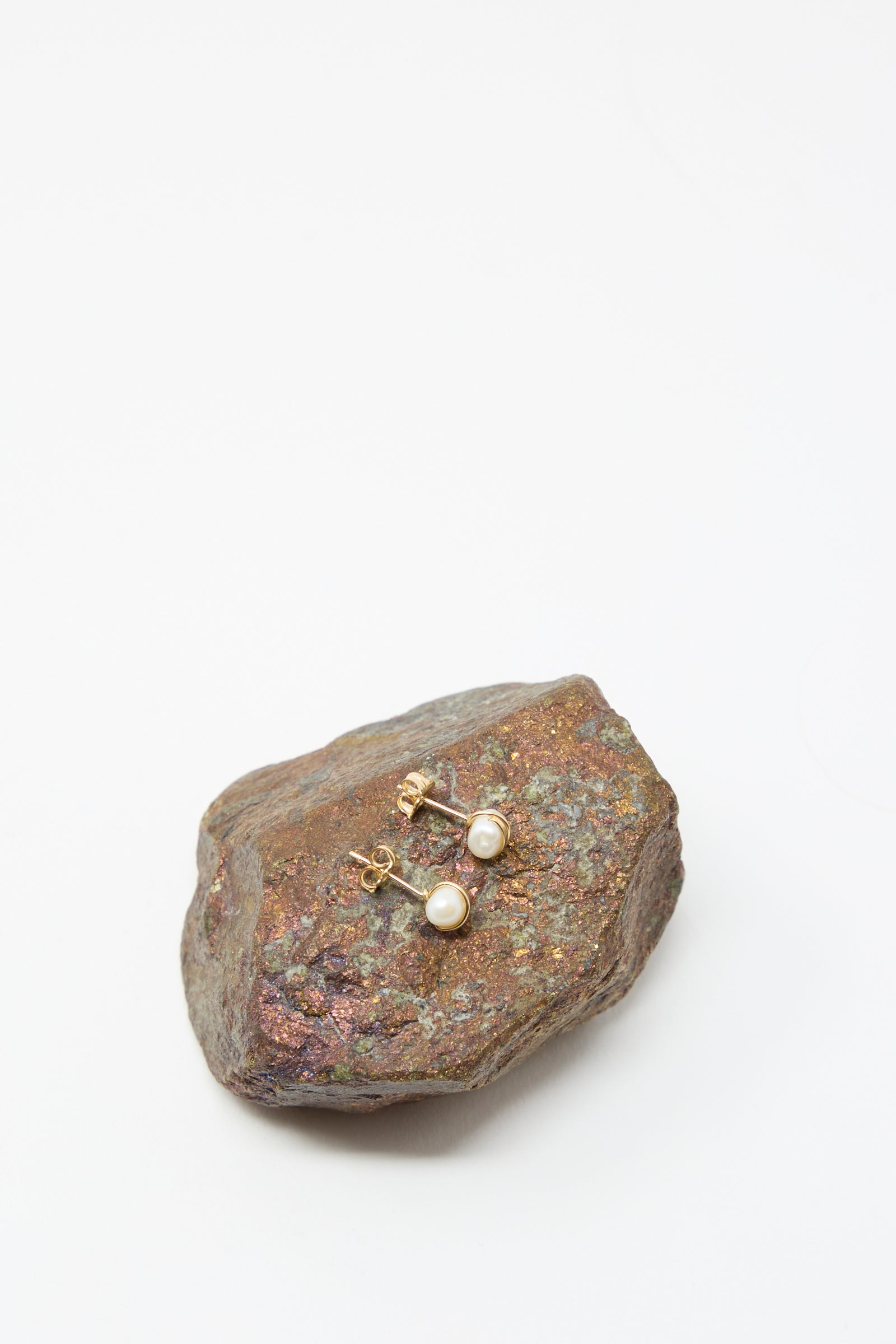 The Mary MacGill Baroque Pearl Studs in White are displayed on a textured, multicolored rock set against a plain white background.