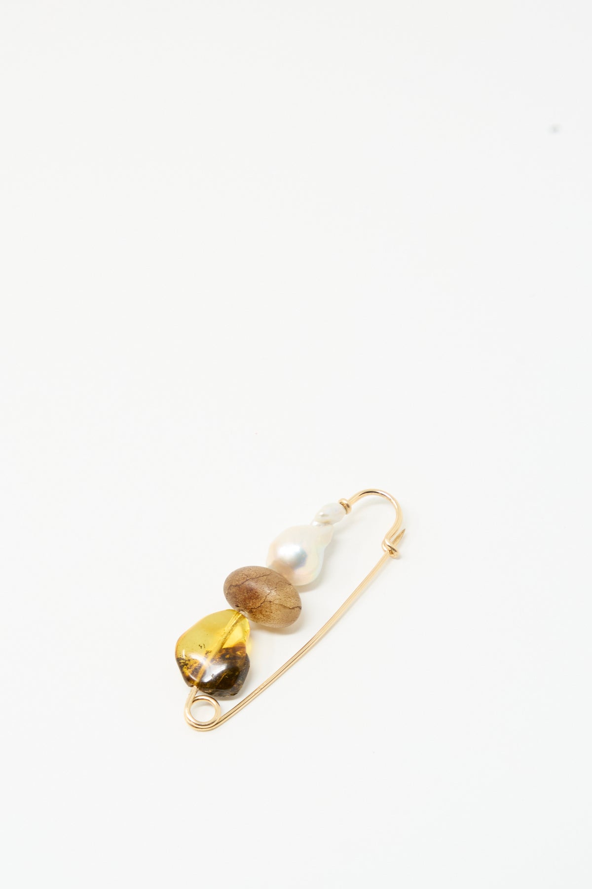 The Frosted Oak Pin by Mary MacGill features a gold safety pin with a yellow stone, baroque pearl, brown translucent bead, and gold-filled wire on a white background.