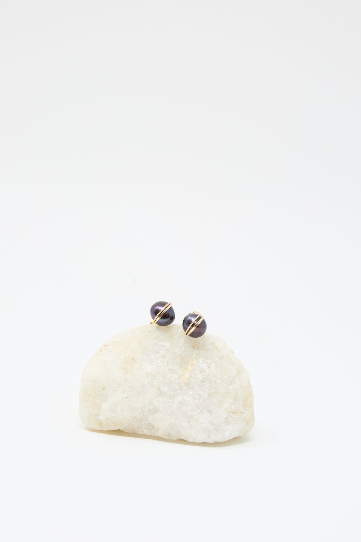 Grande Baroque Pearl Studs in Charcoal by Mary MacGill shown on a white stone, featuring round charcoal pearls with gold accents against a plain white background.