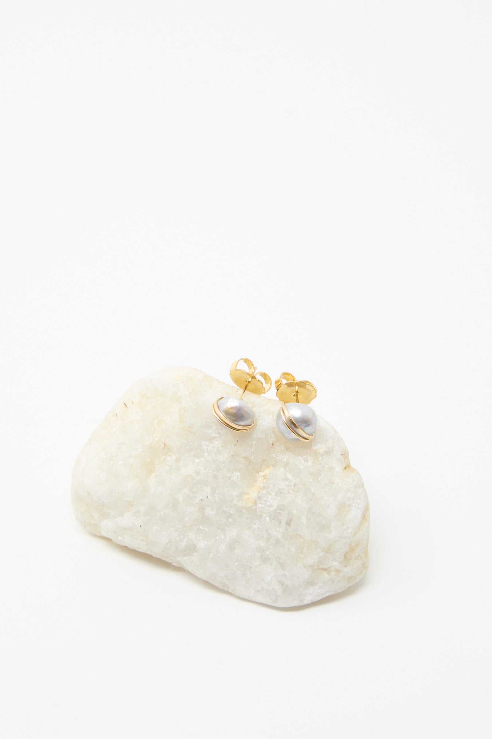 Mary MacGill Grande Baroque Pearl Studs in Silver, handcrafted with lustrous baroque pearls and silver posts, showcased on a white stone against a plain white background.